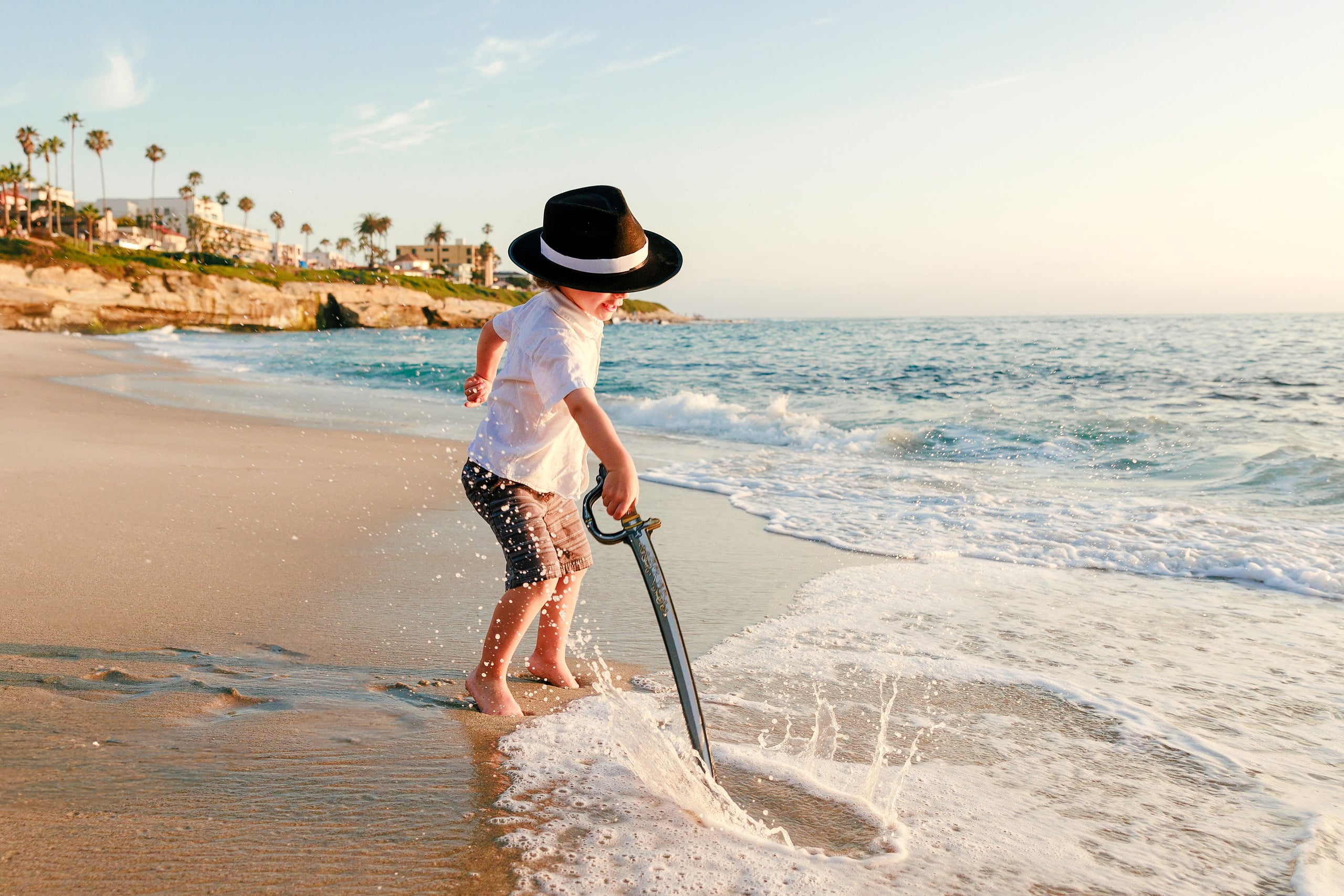 La Jolla Family Photography — 04 Child in shallow water with pirate sword raised at La Jolla during golden hour