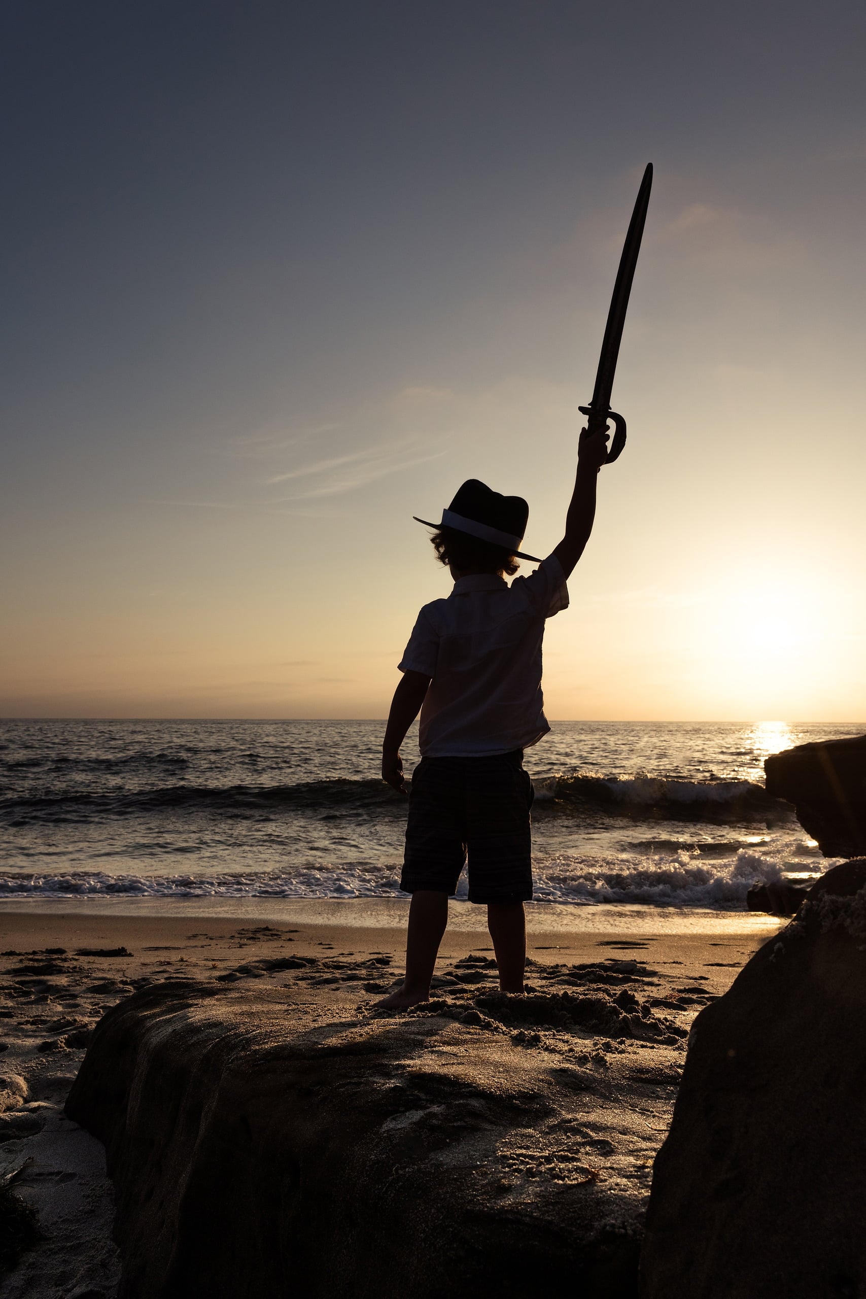 La Jolla Family Photography — 05 Silhouette of child holding pirate sword aloft at sunset over ocean