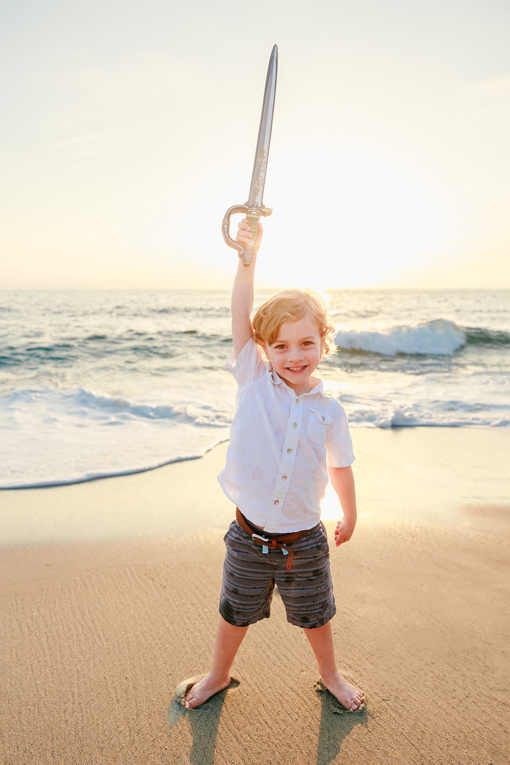 La Jolla Family Photography — 07 Child in white shirt holding sword overhead at sunset on beach