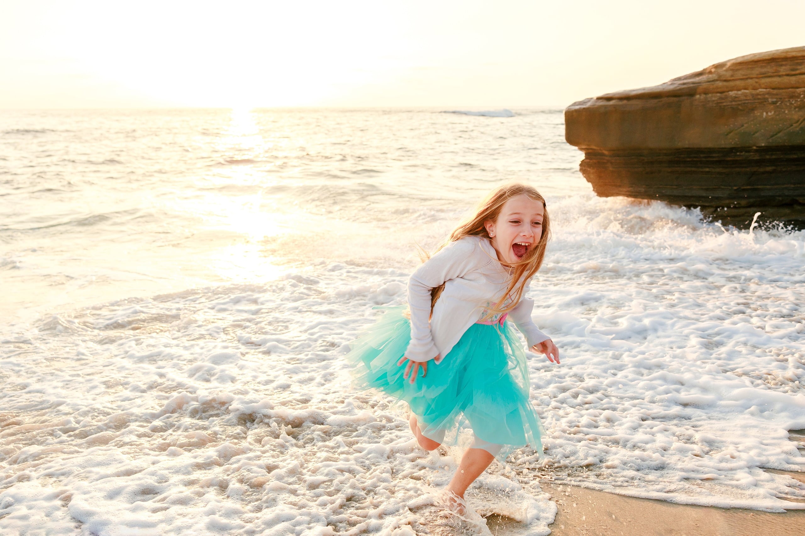 La Jolla Family Photography — 10 Child in turquoise skirt running through shallow water with joyful expression