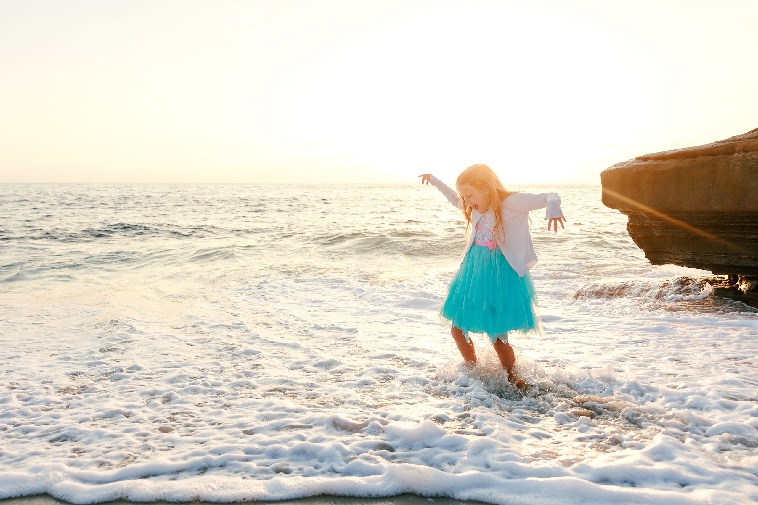 La Jolla Family Photography — 13 Child in turquoise tulle skirt wading in ocean with arms spread wide