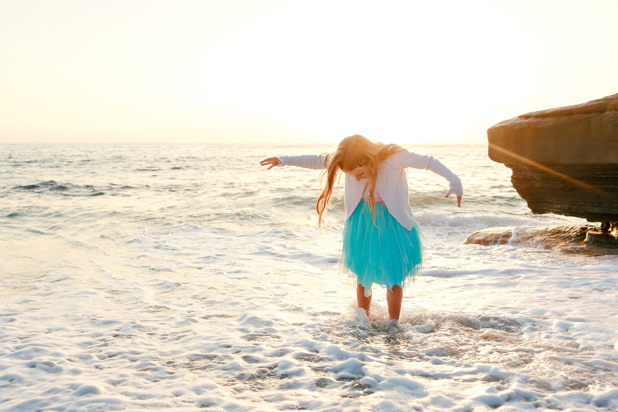La Jolla Family Photography — 14 Child in turquoise skirt posing on beach at golden hour with waves behind