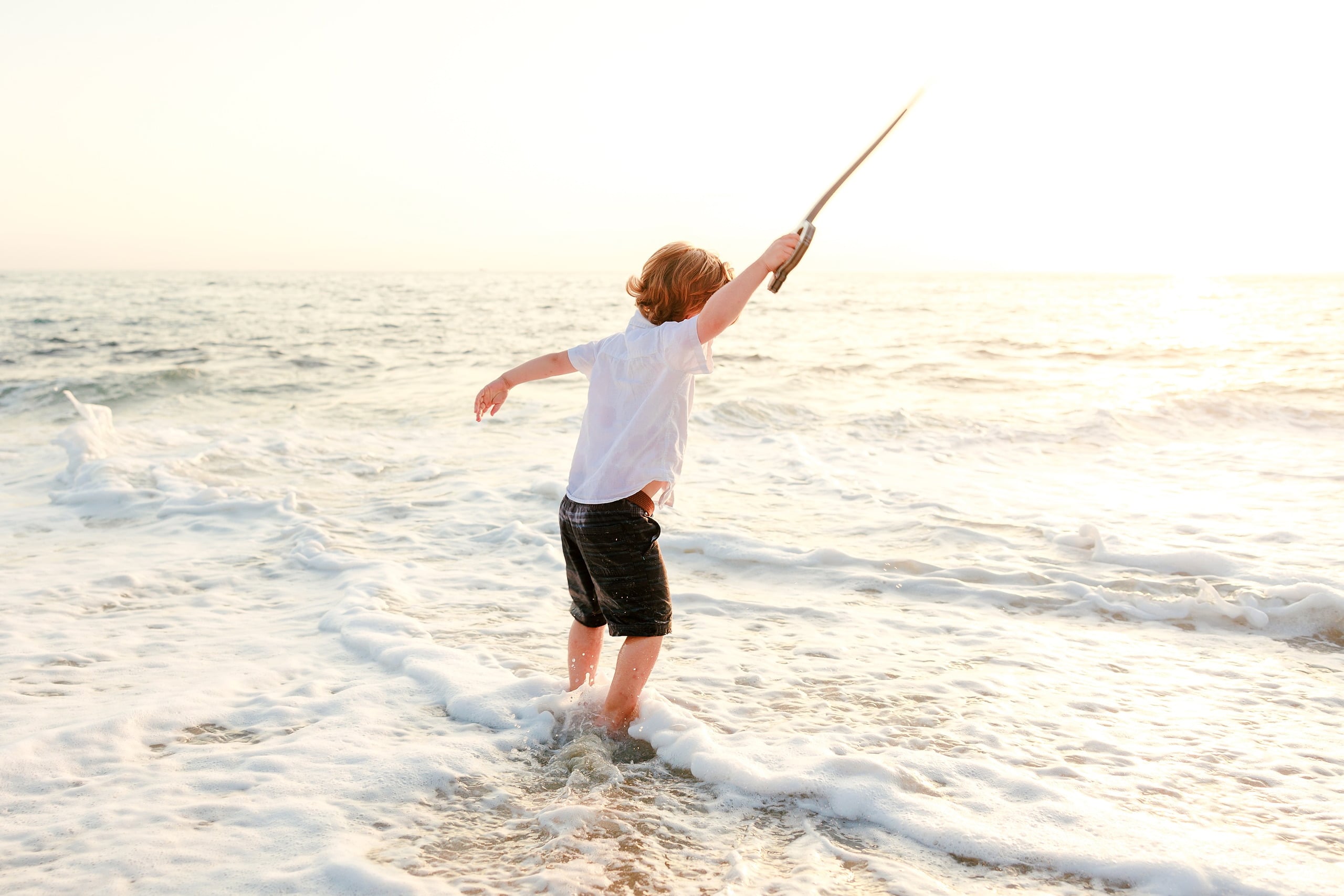 La Jolla Family Photography — 17 Child in white shirt with sword held high wading on beach