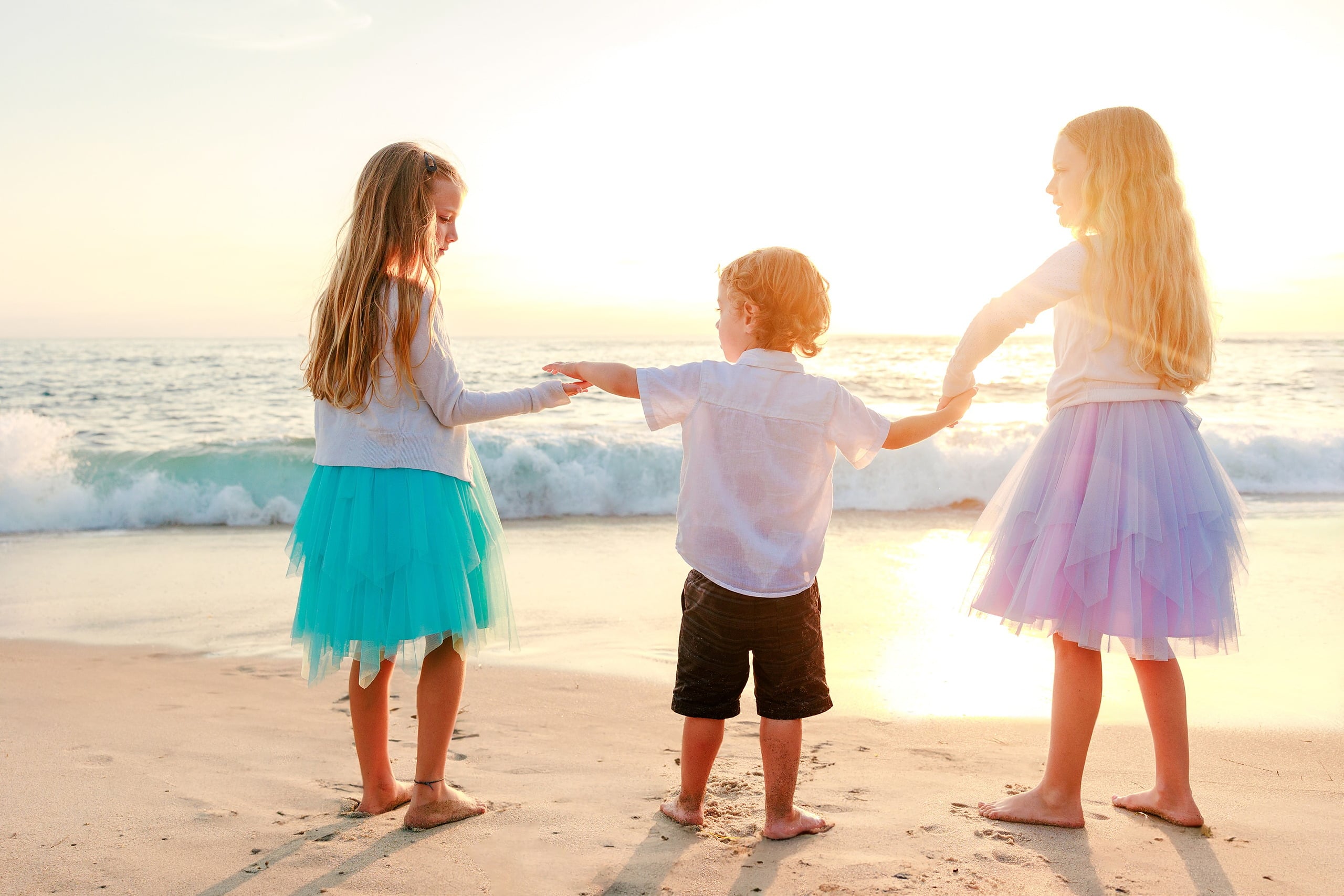 La Jolla Family Photography — 25 Three children holding hands on beach at golden hour, two girls in tutus flanking a toddler in white