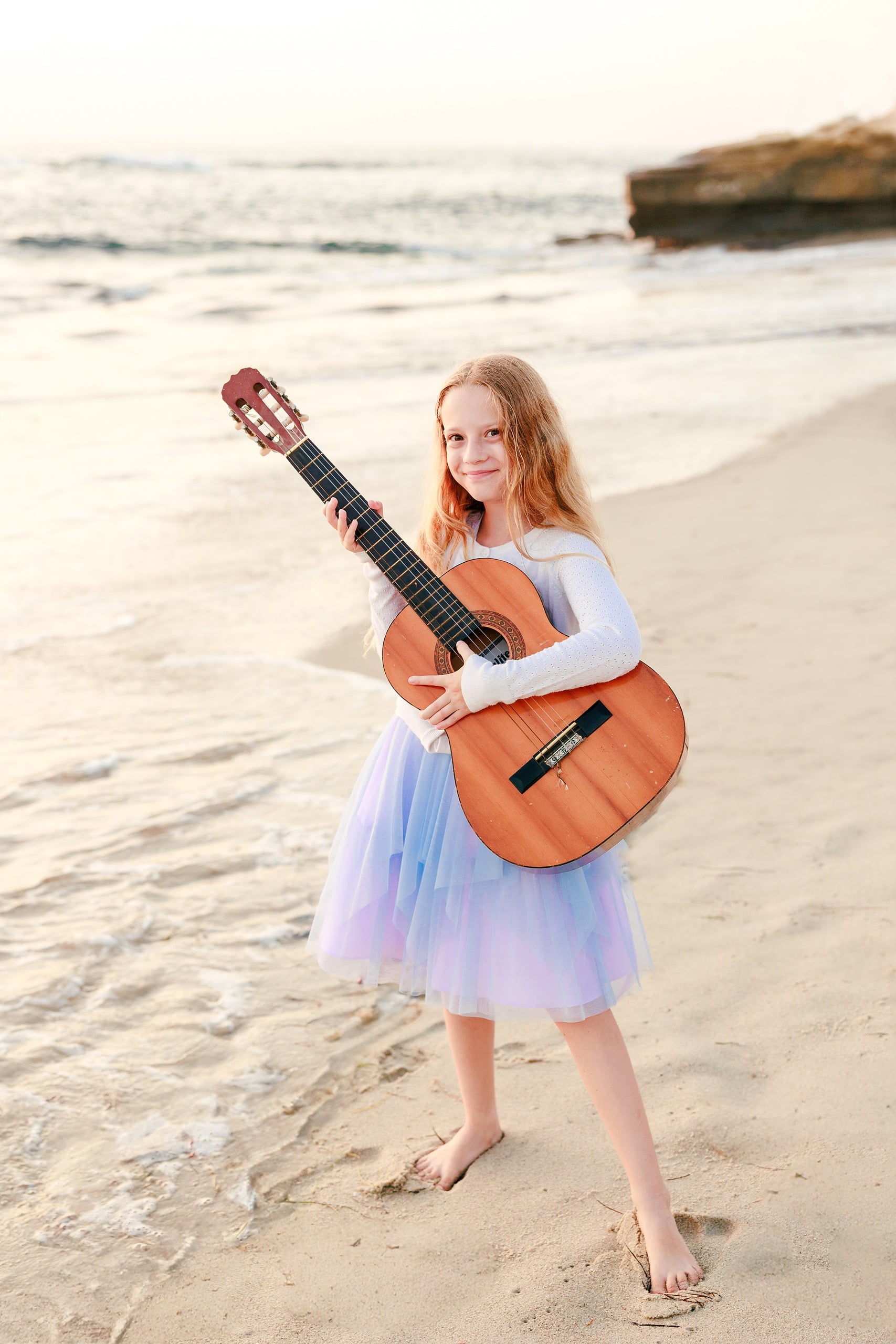 La Jolla Family Photography — 40 Teen girl holding guitar wearing white long-sleeved shirt and purple tulle on beach