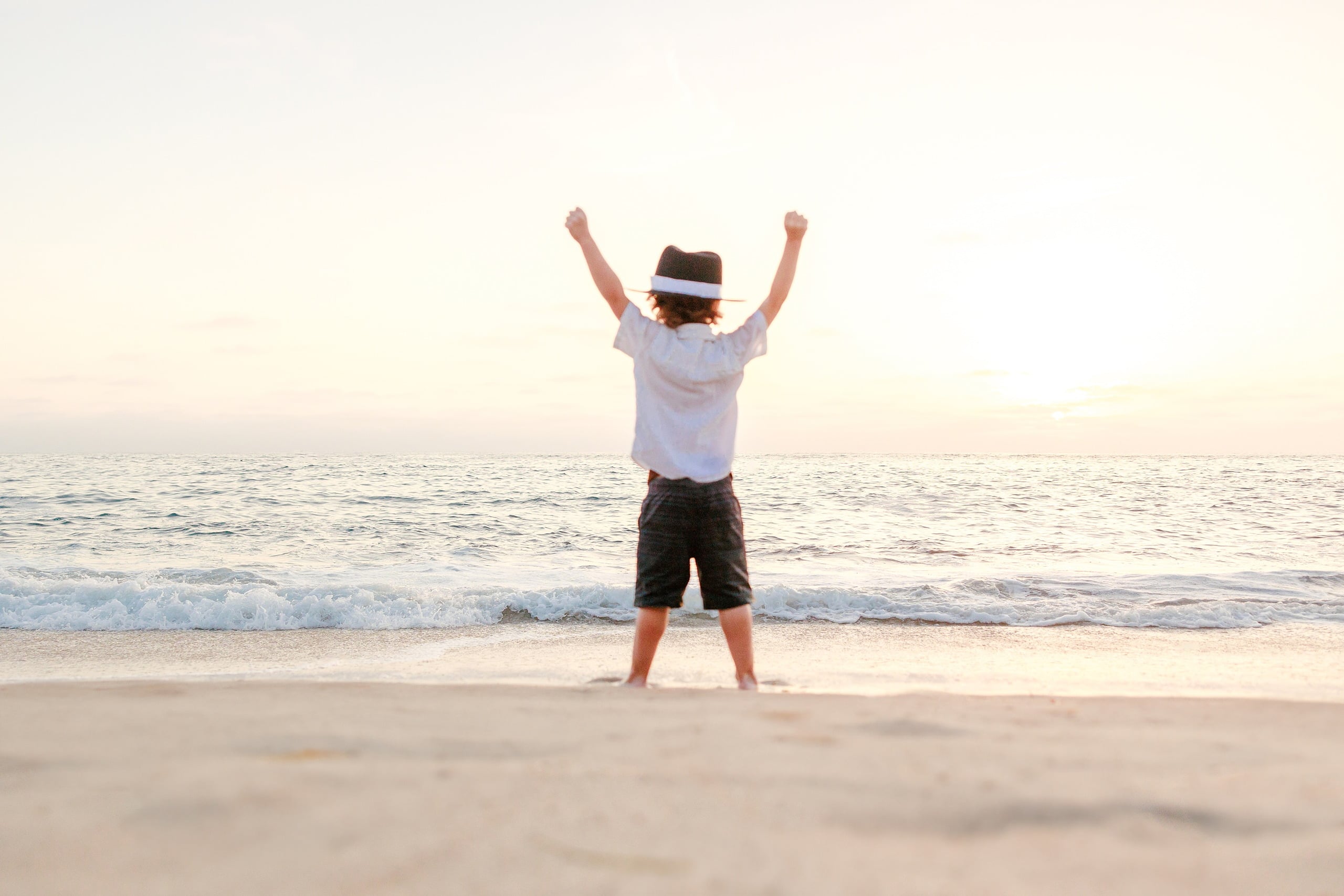 La Jolla Family Photography — 41 Boy in white shirt and black shorts with arms raised at sunset on beach