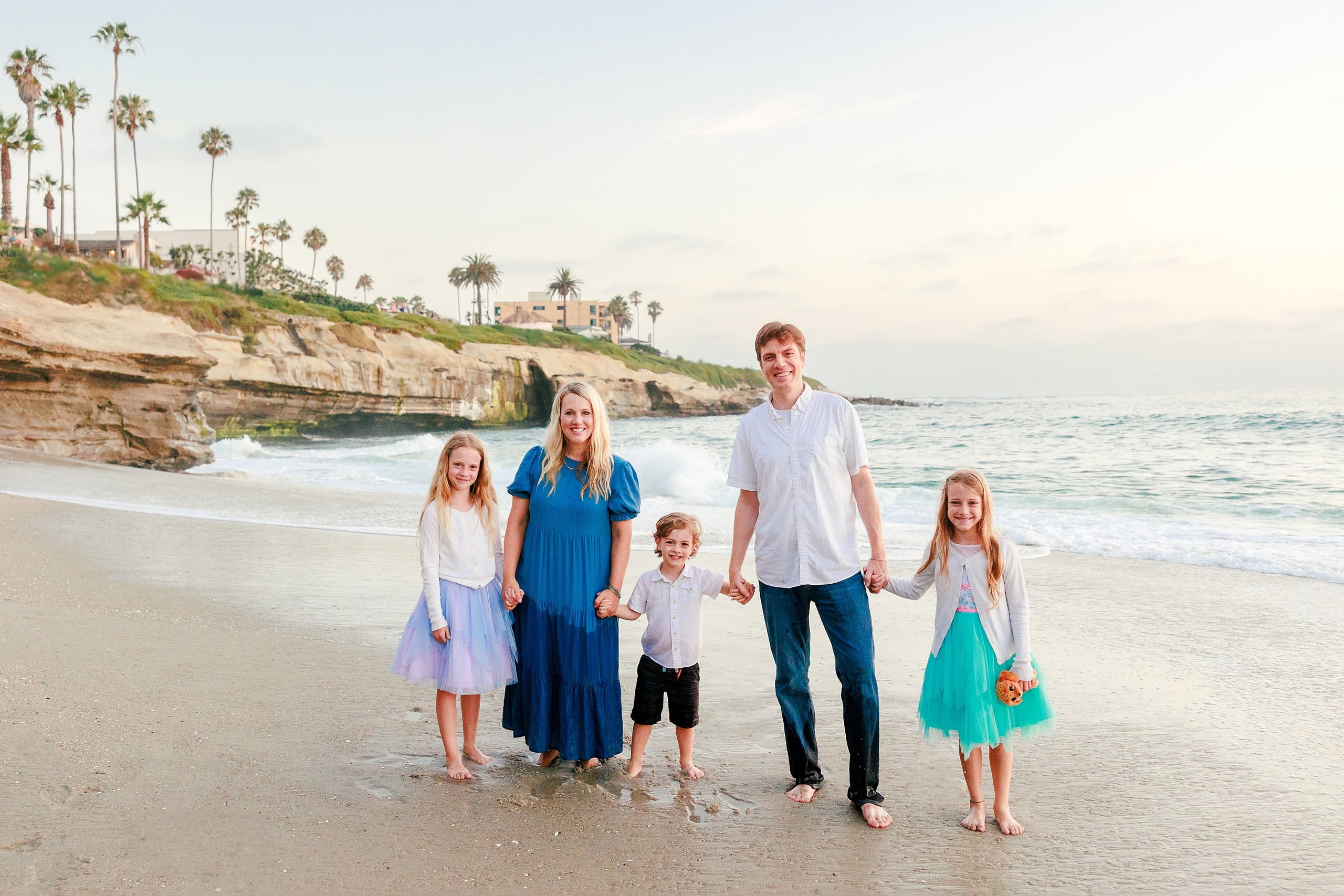 La Jolla Family Photography — 50 Family posing in shallow water on beach with palm tree bluff visible