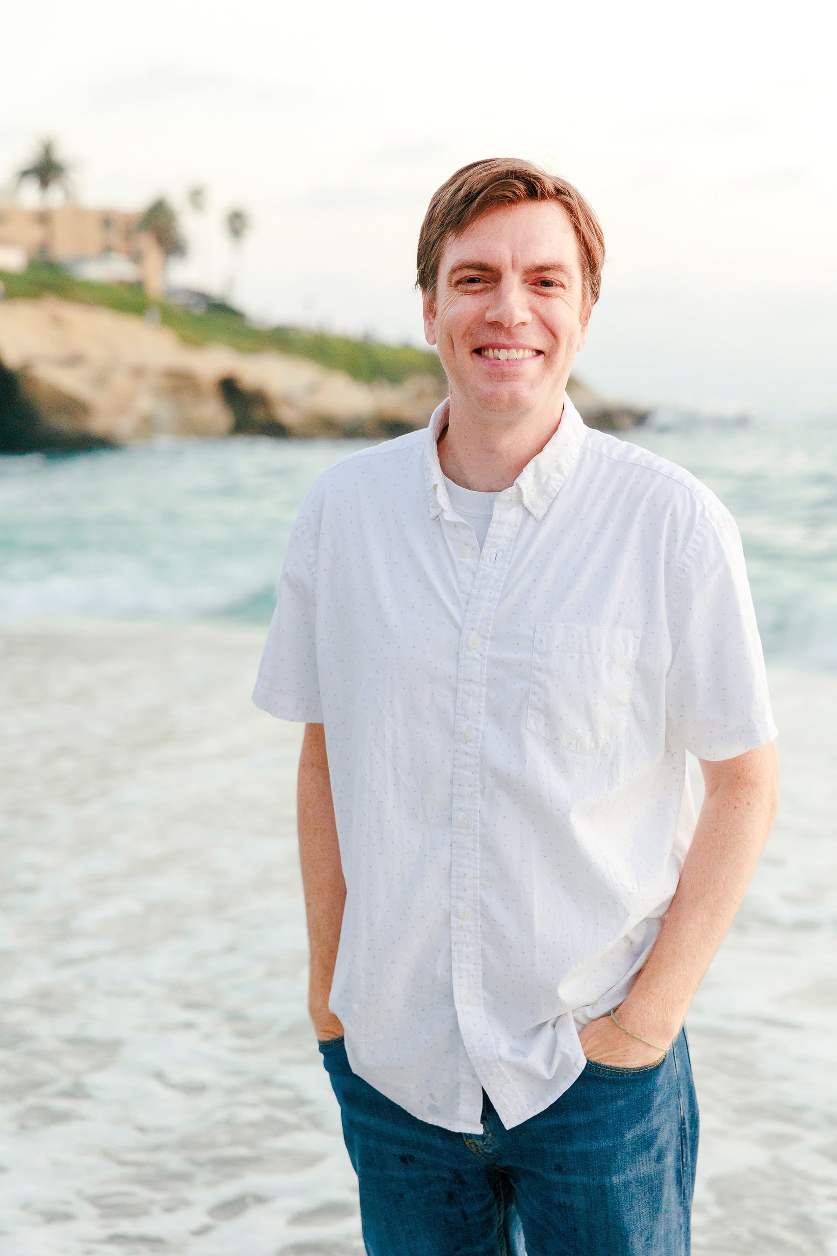 La Jolla Family Photography — 51 Adult man in white button-up shirt smiling on beach against ocean backdrop