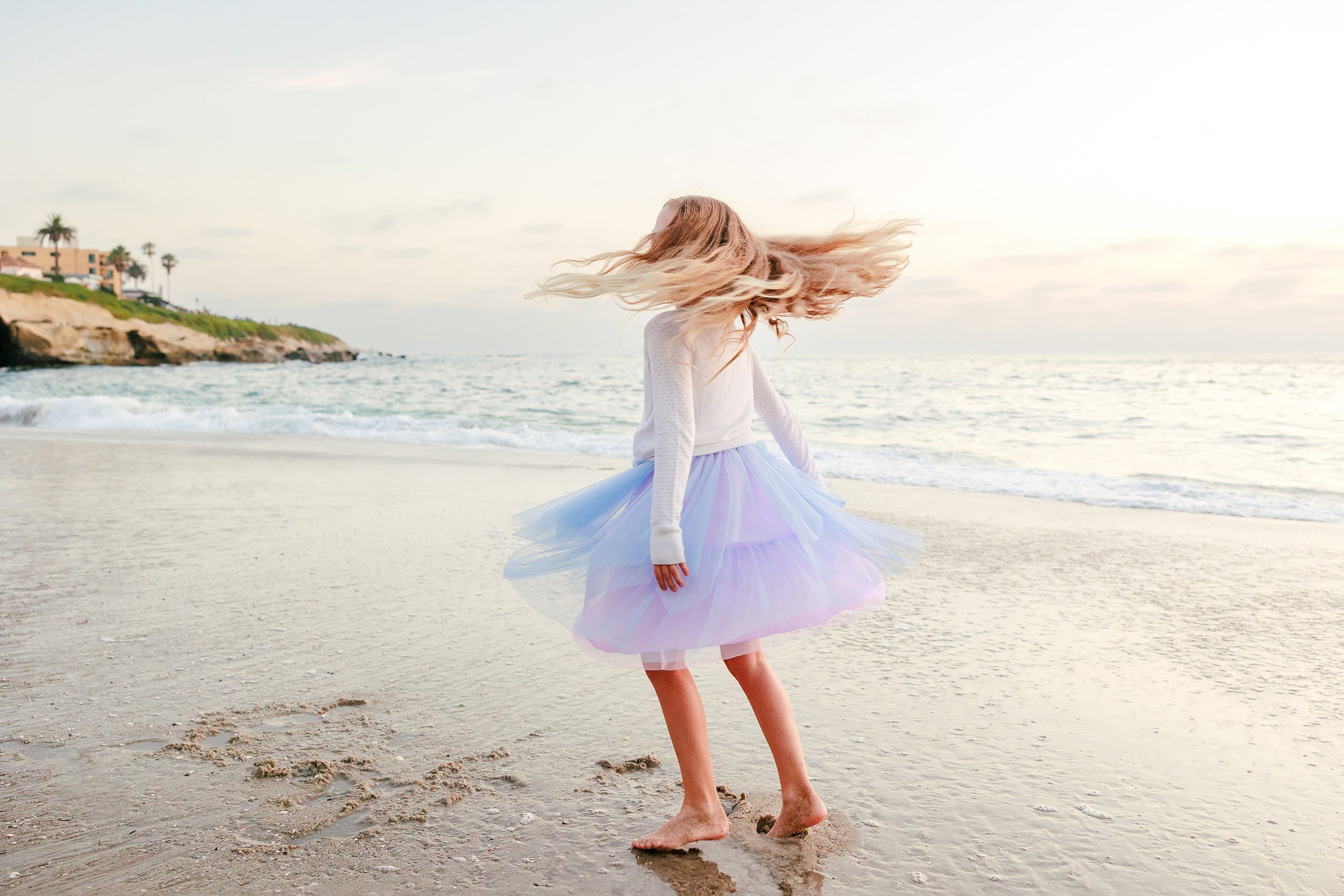 La Jolla Family Photography — 56 Girl in white and light purple tulle spinning on beach, hair in motion