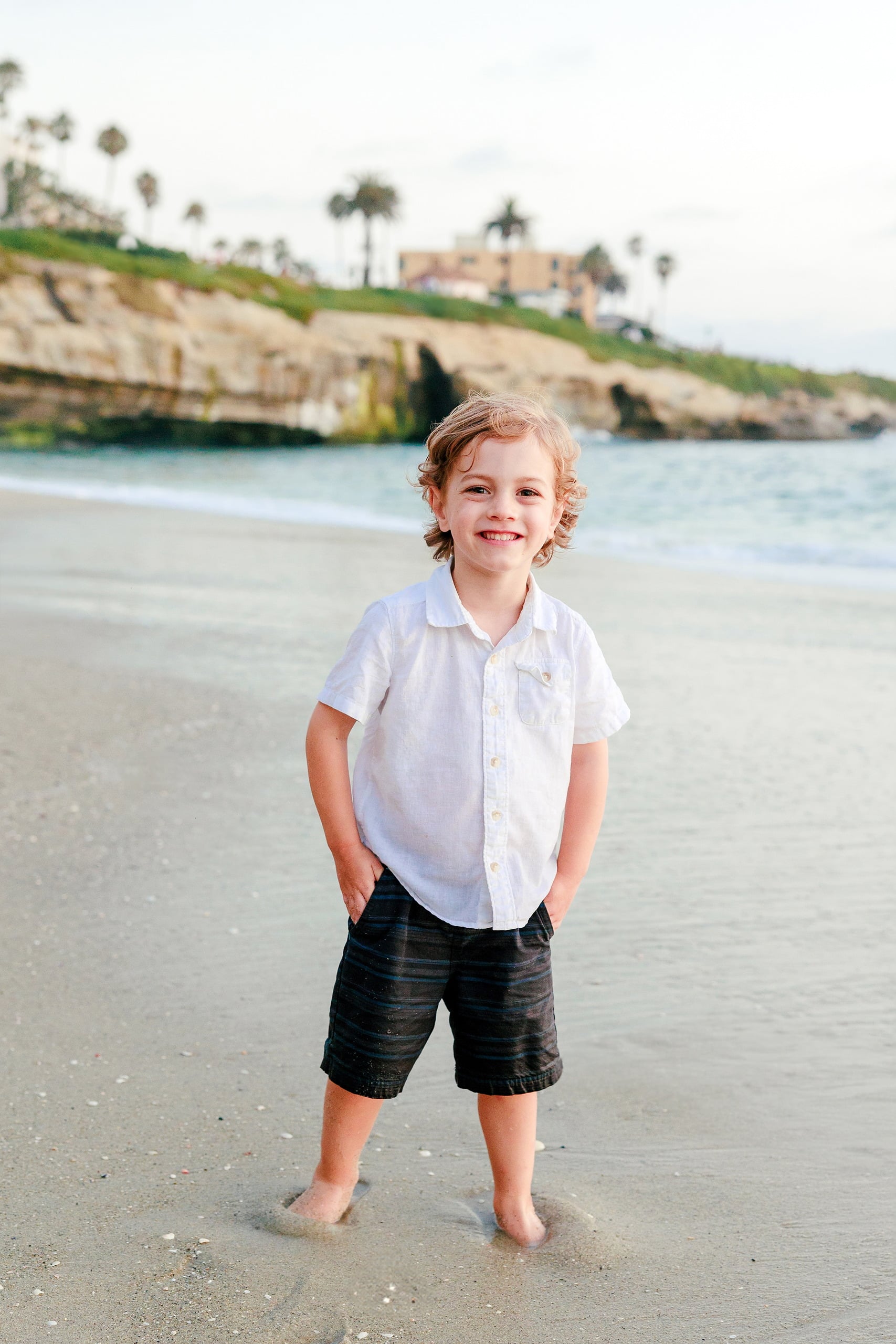 La Jolla Family Photography — 59 Young boy in white shirt and black shorts posing on beach at La Jolla