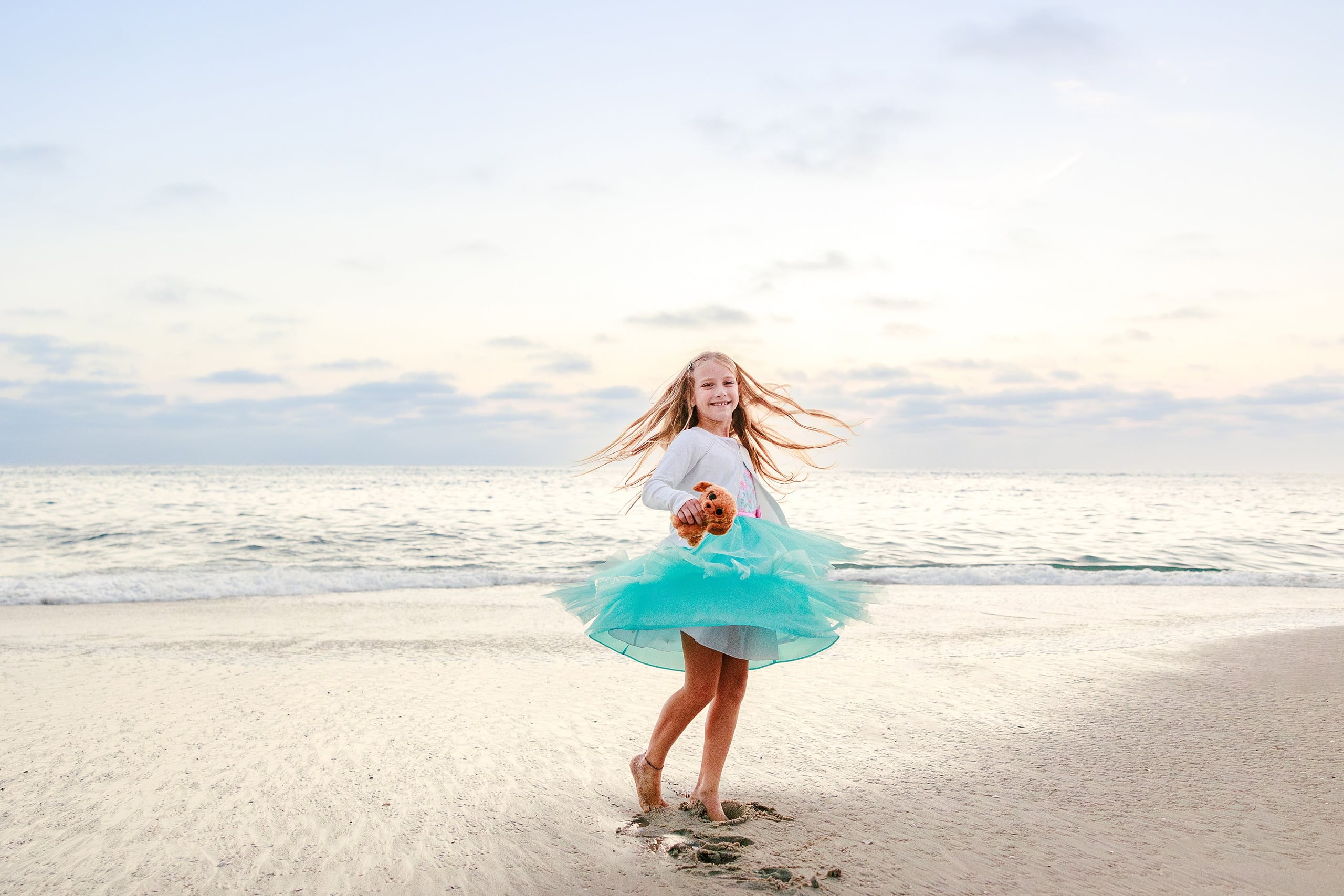 La Jolla Family Photography — 69 Girl in white and turquoise tulle spinning on beach holding teddy bear
