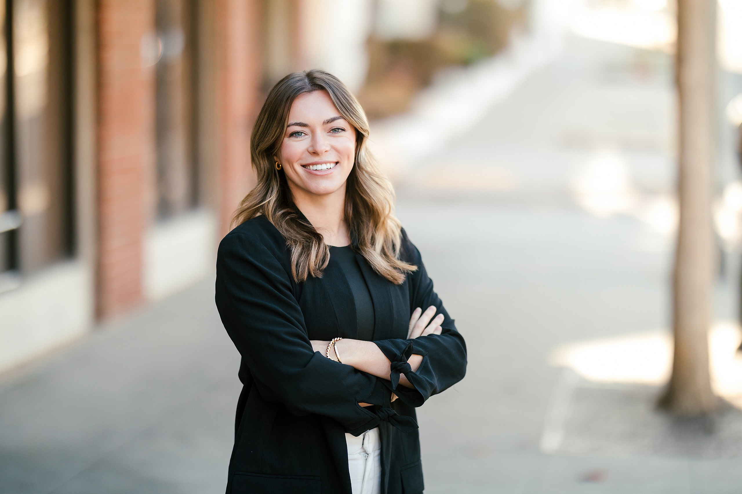 Lauren Headshots in La Mesa — 01 Lauren stands with arms crossed on an urban street in La Mesa with brick building behind