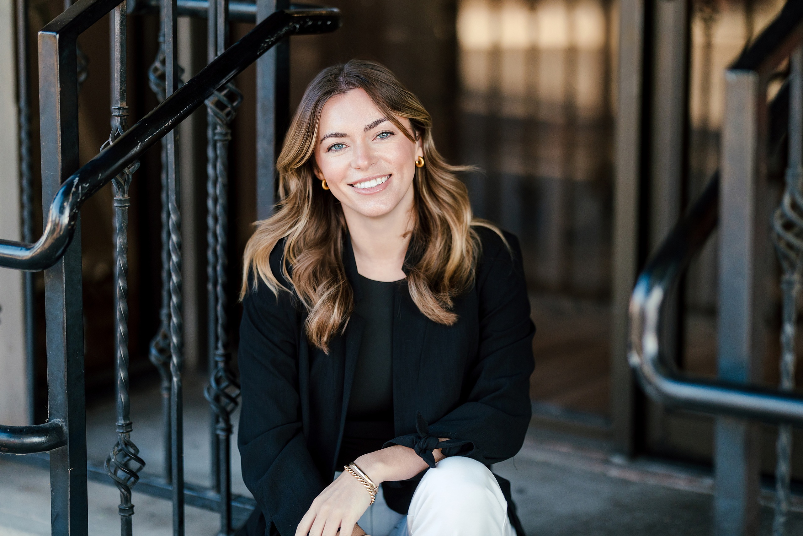Lauren Headshots in La Mesa — 02 Woman sits on decorative metal stairs with hand on railing in an urban outdoor setting