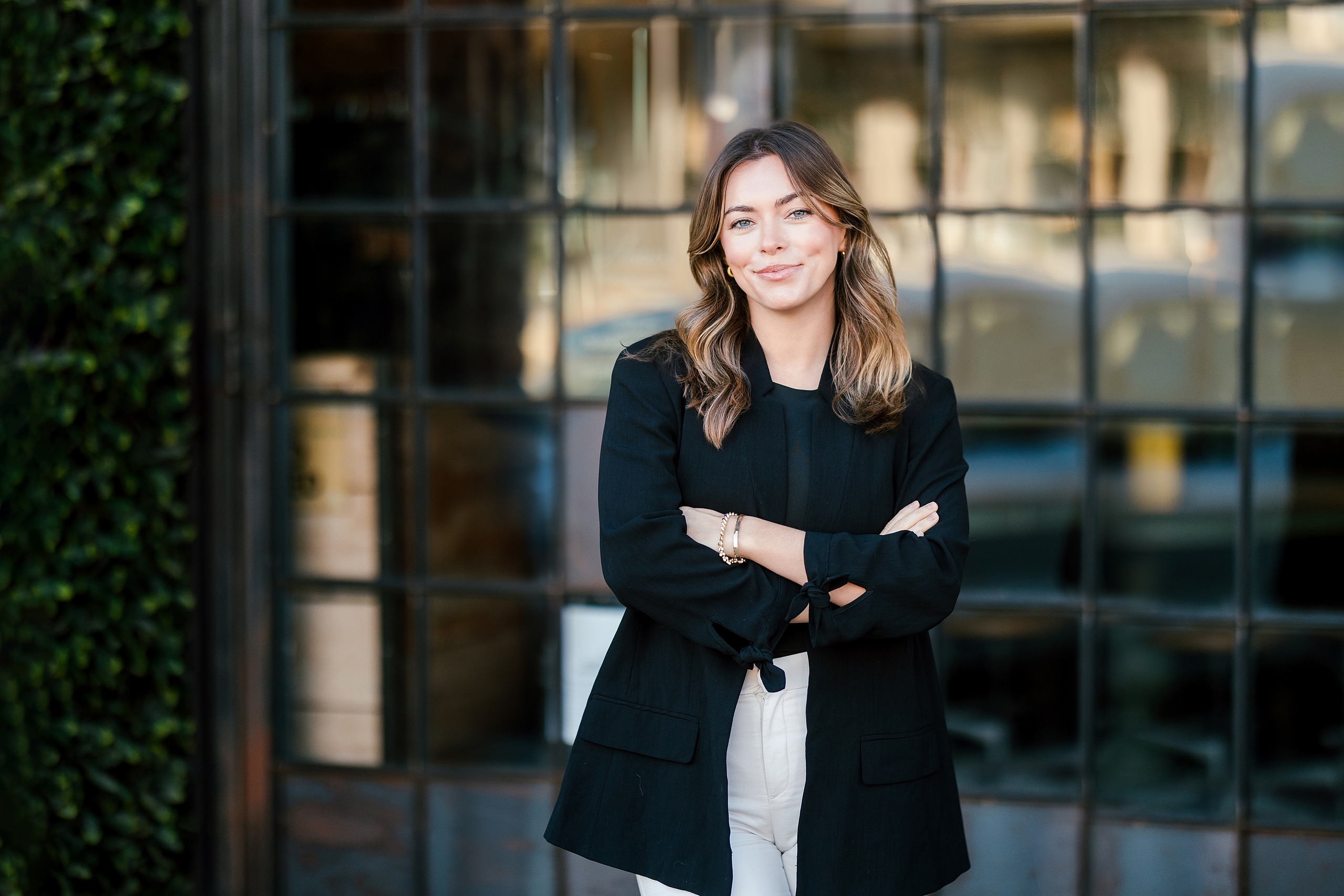 Lauren Headshots in La Mesa — 07 Woman stands with arms crossed against a modern building with geometric windows and ivy vines