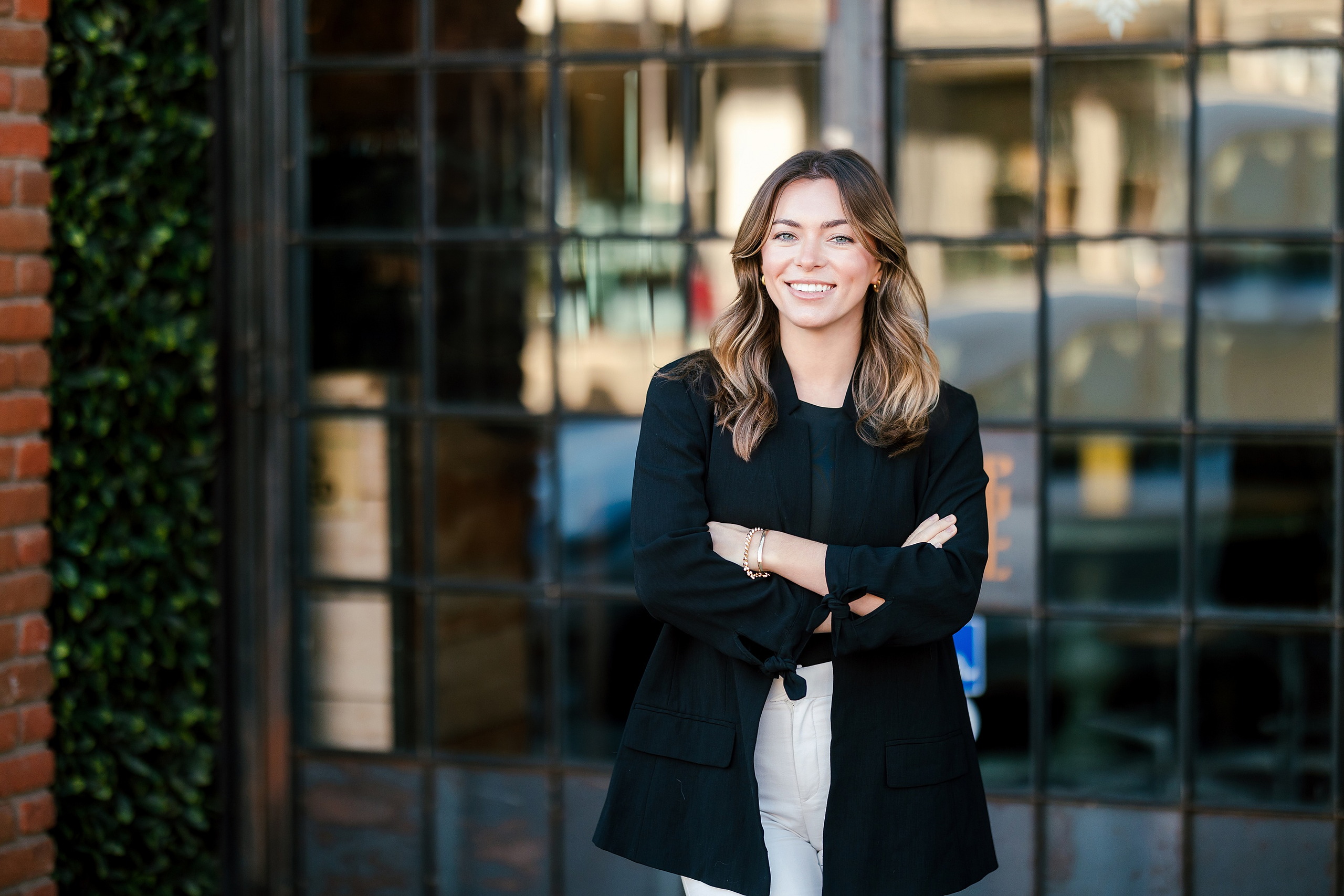 Lauren Headshots in La Mesa — 08 Professional woman stands arms crossed in front of a glass building with red brick and ivy
