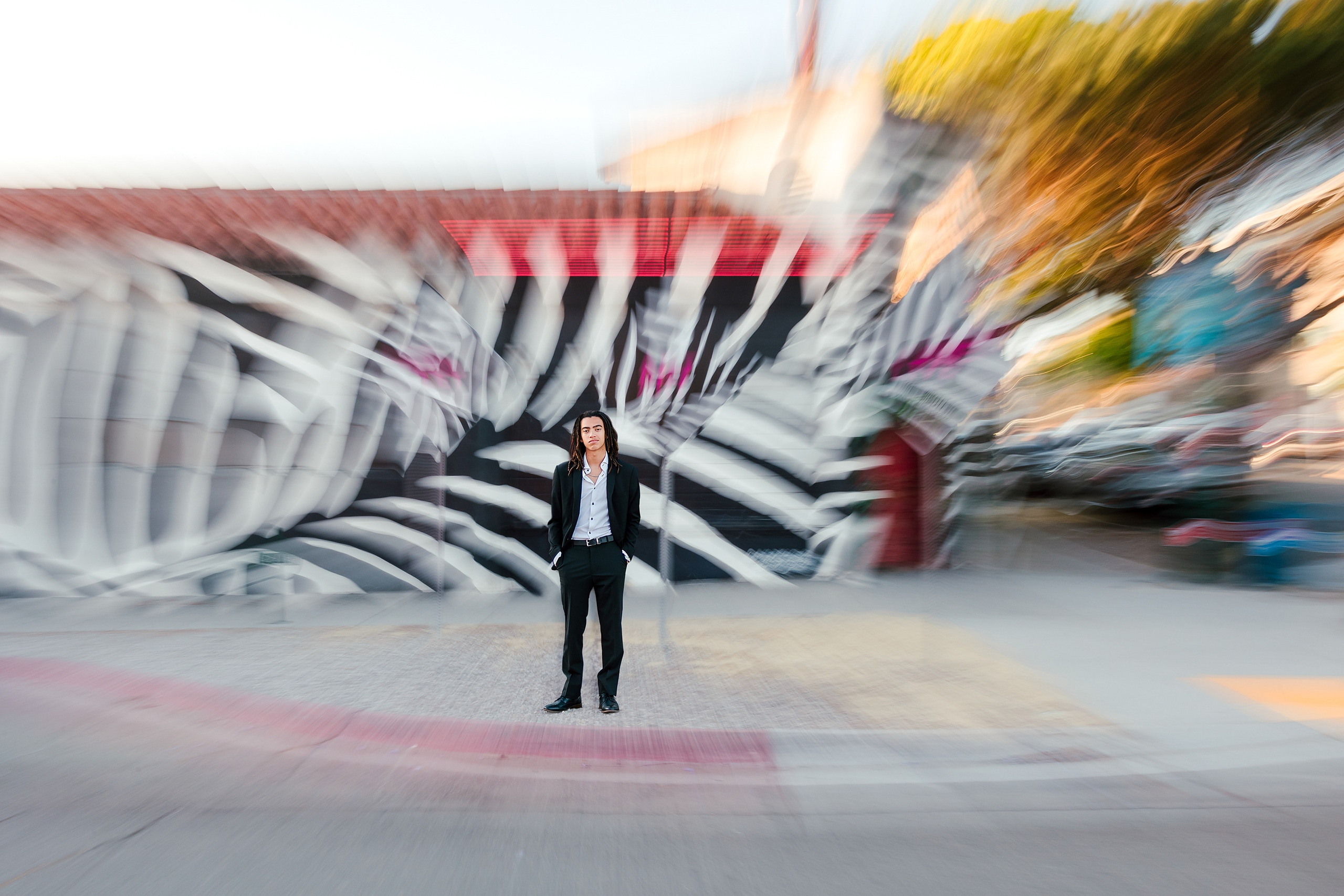 Little Italy Senior Photos — 01 Joshua stands in motion in front of colorful mural on Little Italy street