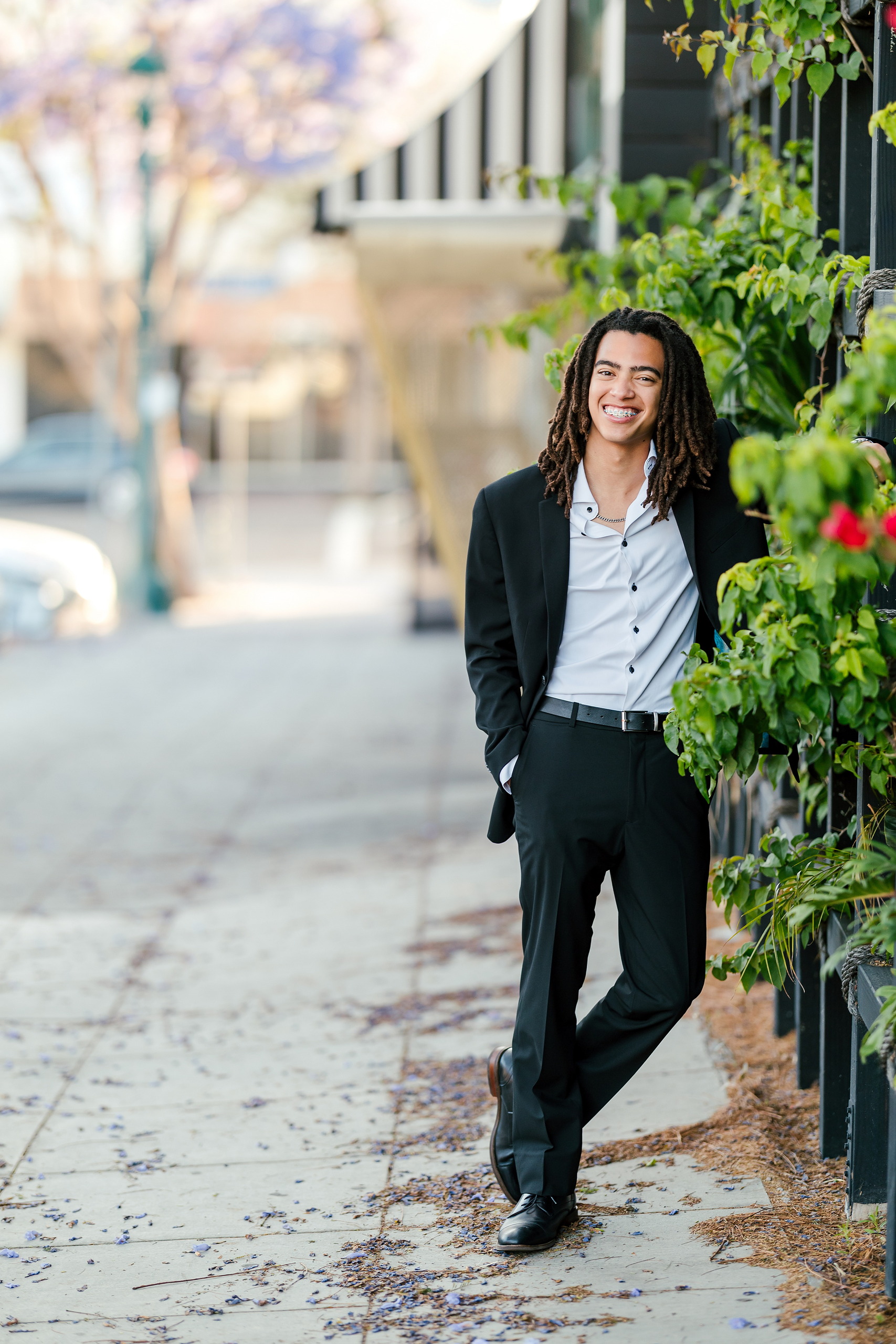 Little Italy Senior Photos — 05 Joshua smiling among red flowers and climbing ivy on building