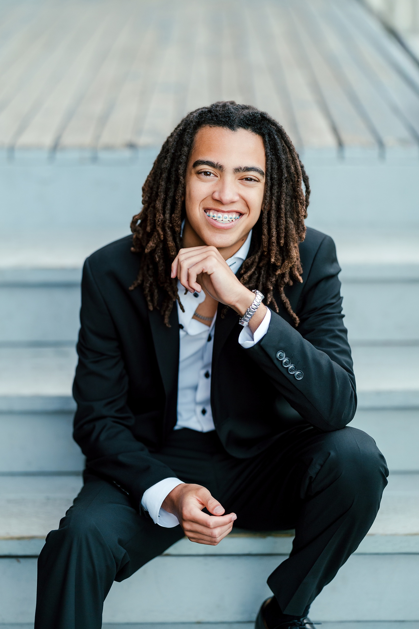 Little Italy Senior Photos — 12 Joshua crouching and smiling against water and metal stair backdrop