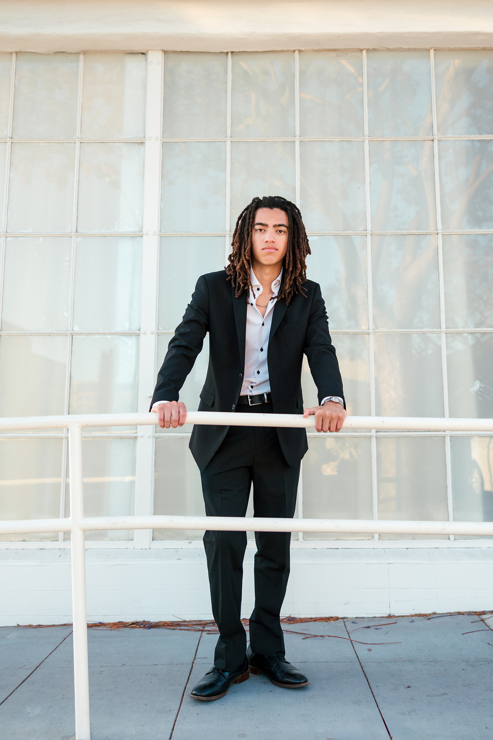 Little Italy Senior Photos — 13 Joshua holding railing against large industrial windows in golden light