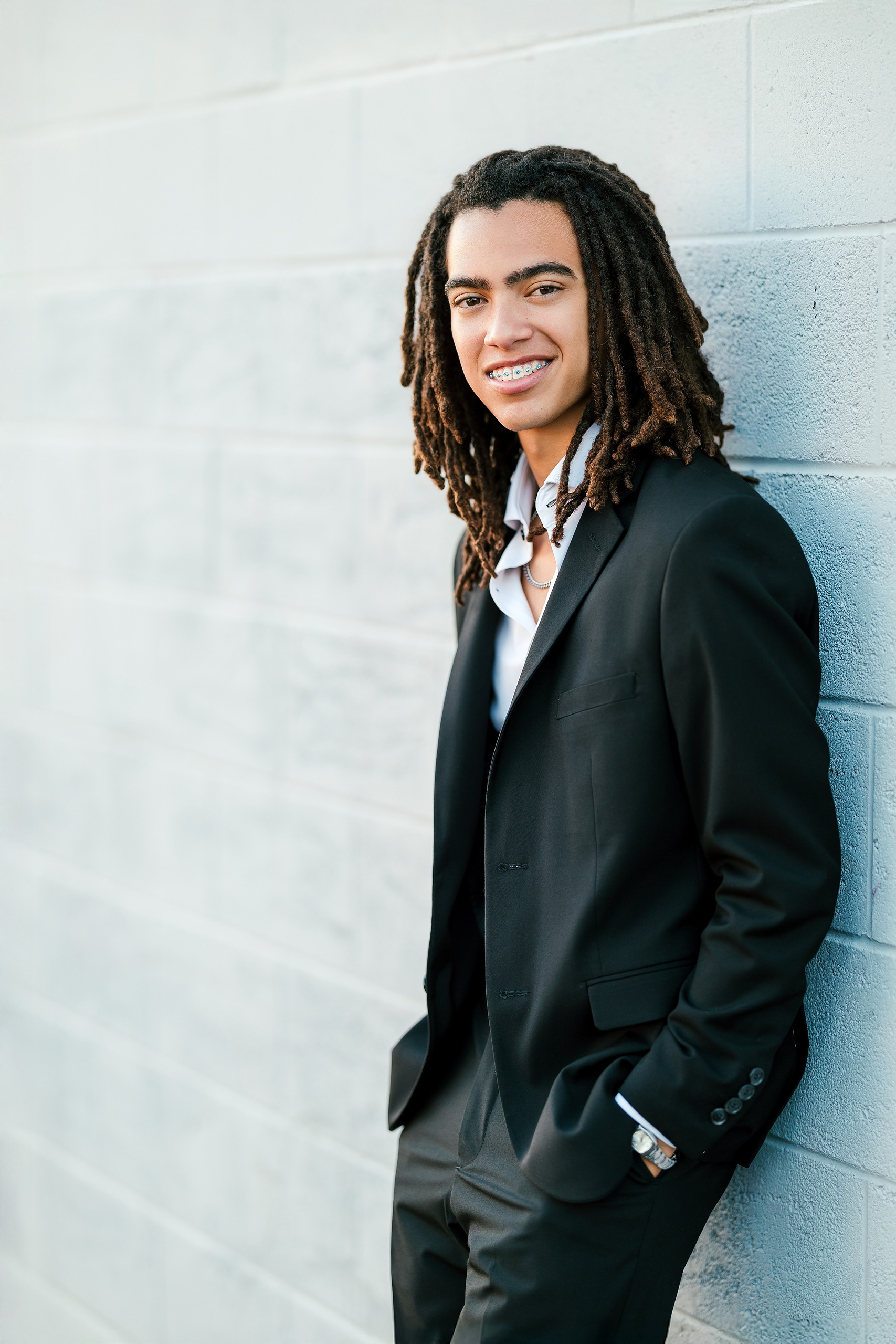 Little Italy Senior Photos — 15 Joshua smiling in black suit against minimalist concrete wall
