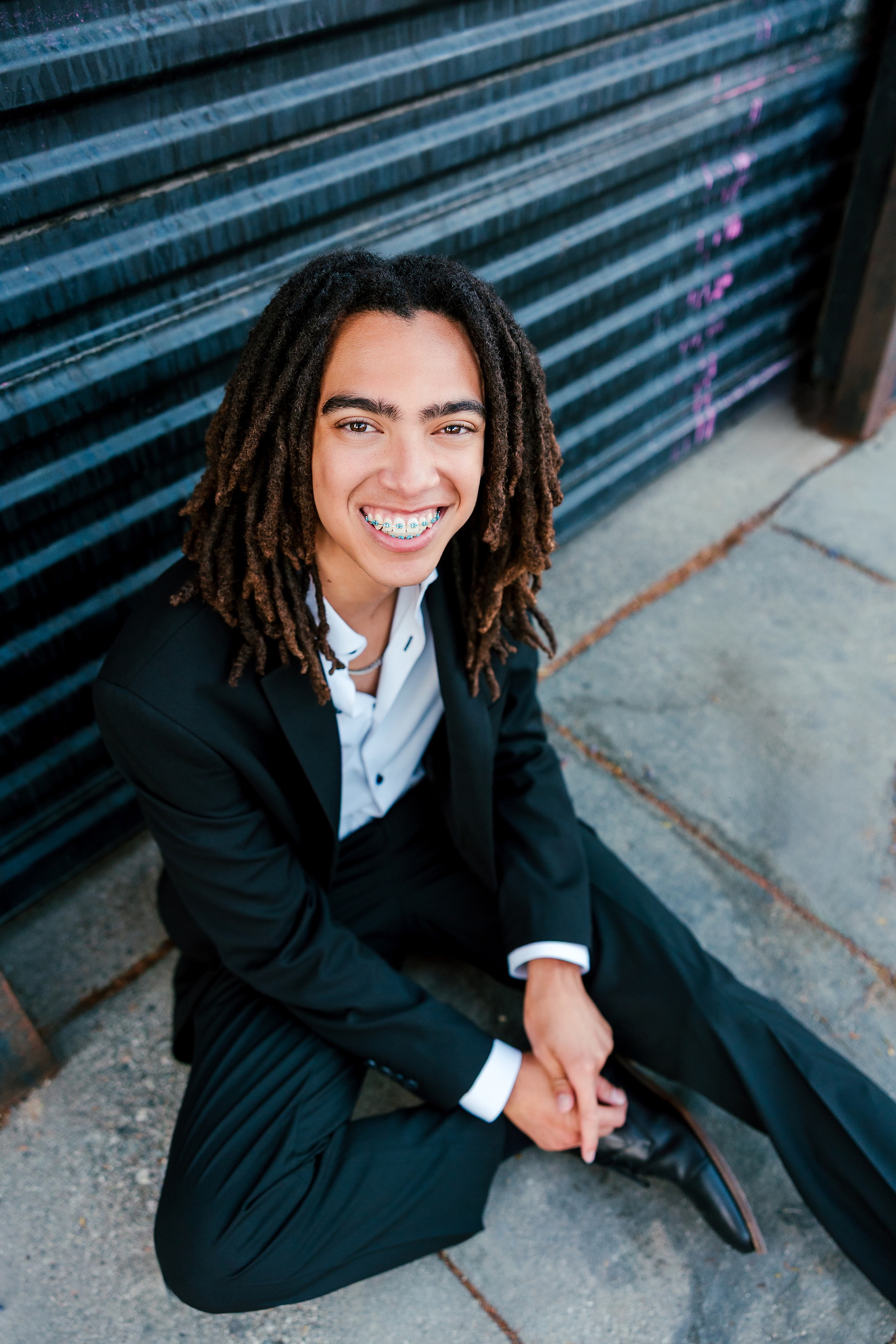 Little Italy Senior Photos — 17 Joshua standing confidently with soft-focus urban background at dusk