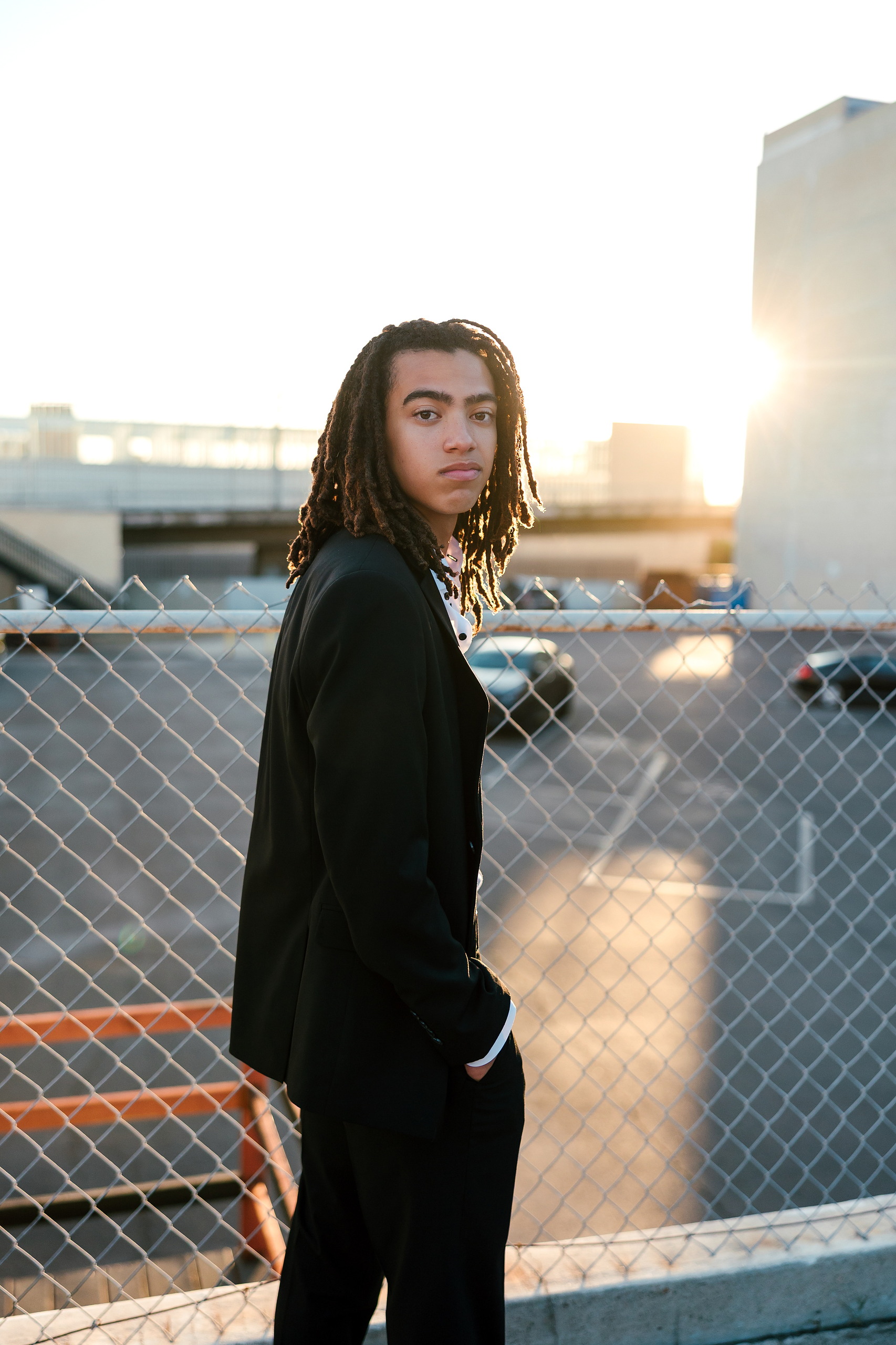 Little Italy Senior Photos — 19 Joshua turning to look back in sunset light against chain-link fence