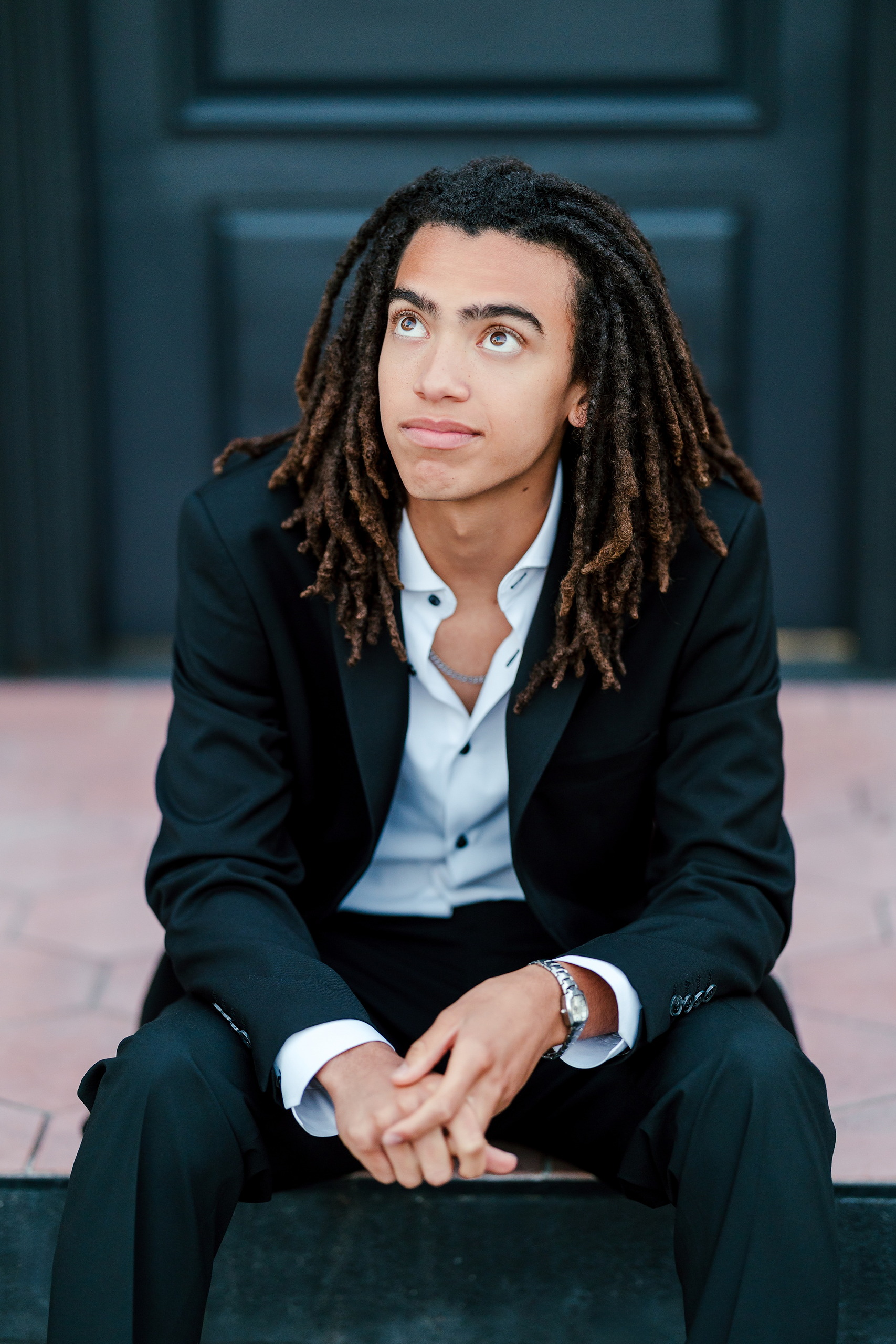Little Italy Senior Photos — 21 Joshua crouching and gazing away against dark teal painted wall