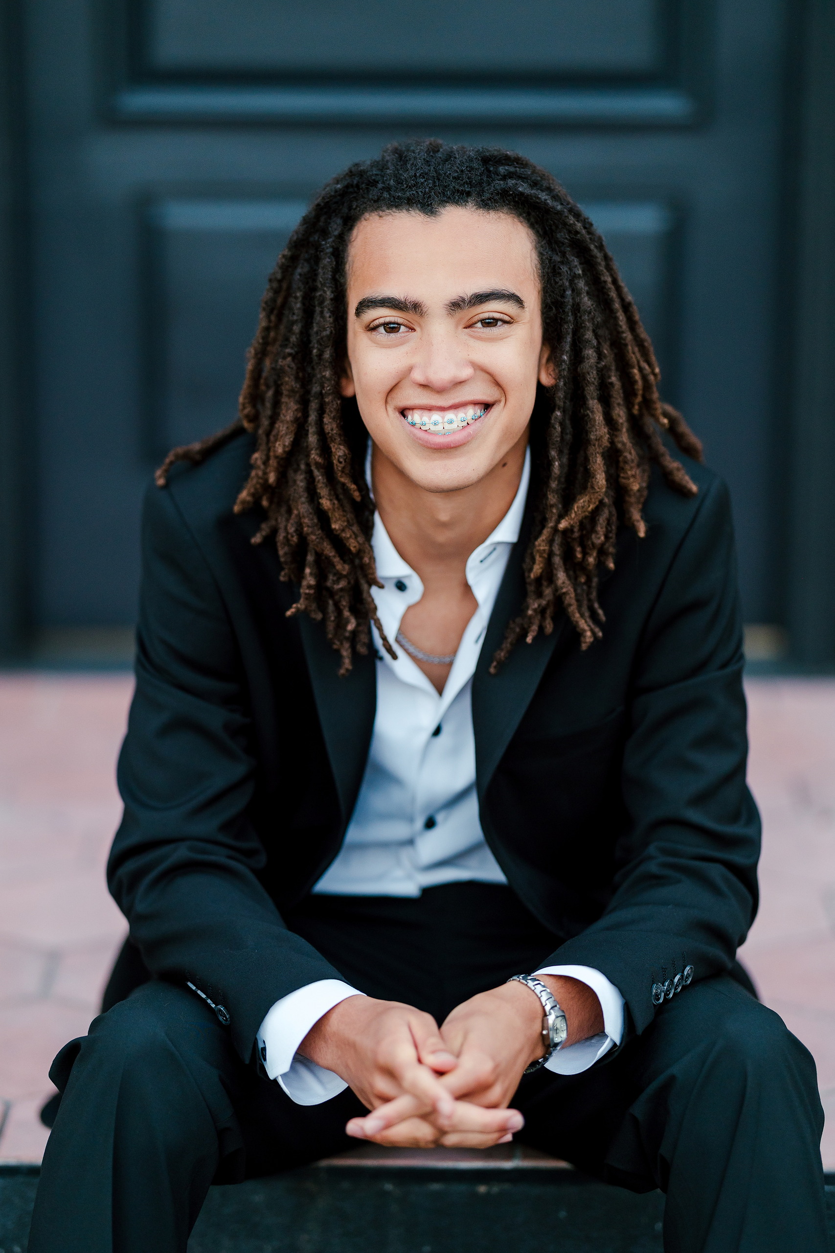 Little Italy Senior Photos — 24 Joshua crouching and beaming with joy against dark teal wall