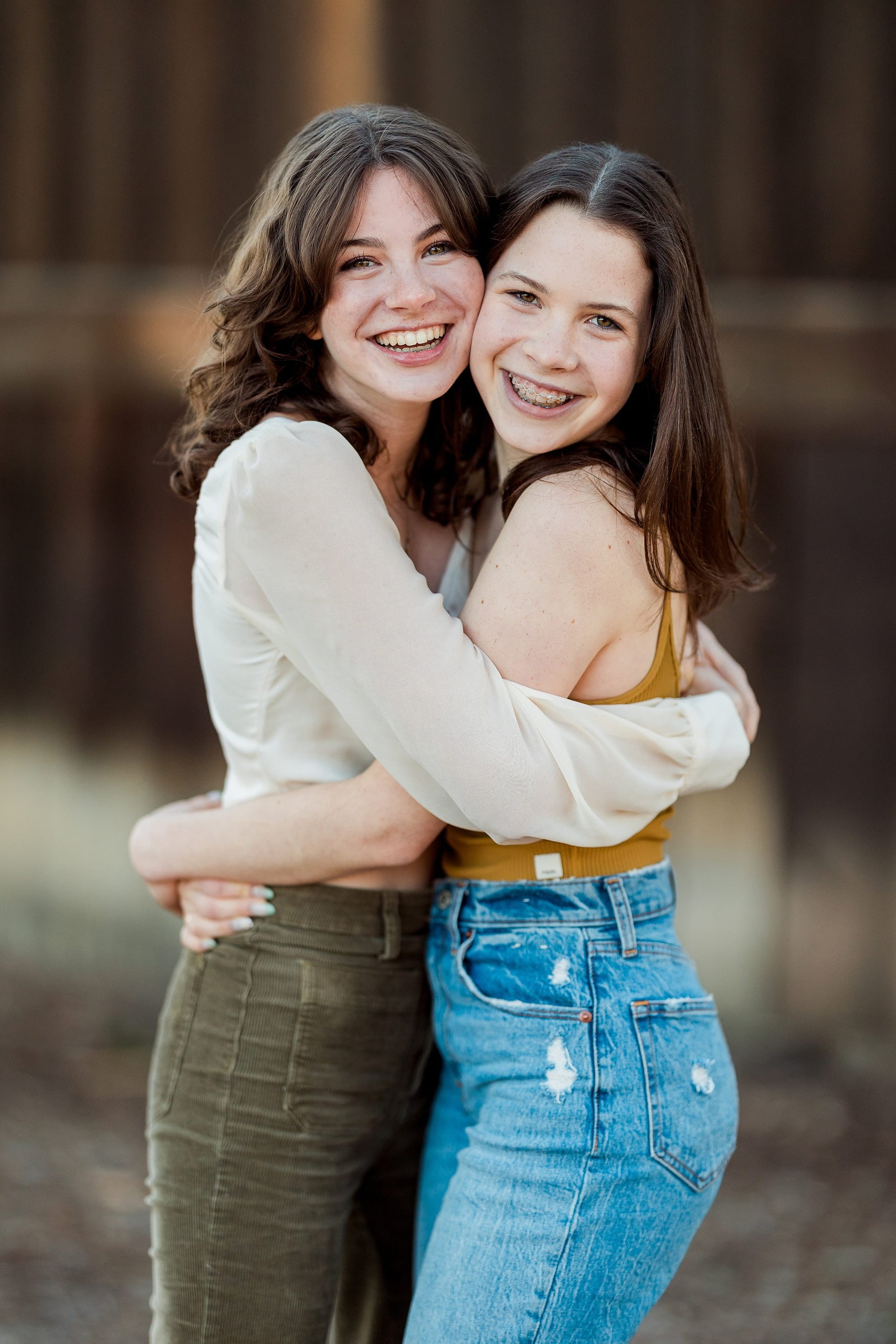 Photographer San Diego — 11 Two sisters holding each other and smiling at wooden backdrop