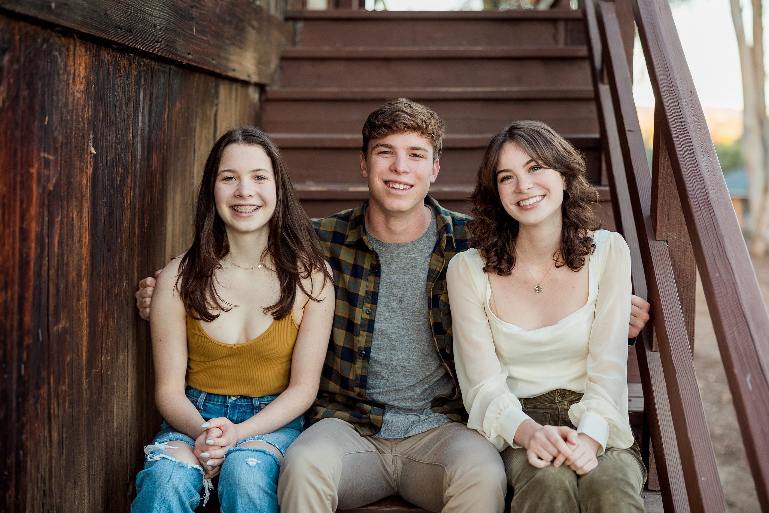 Photographer San Diego — 29 Three teen siblings sitting together on wooden stairs at outdoor venue