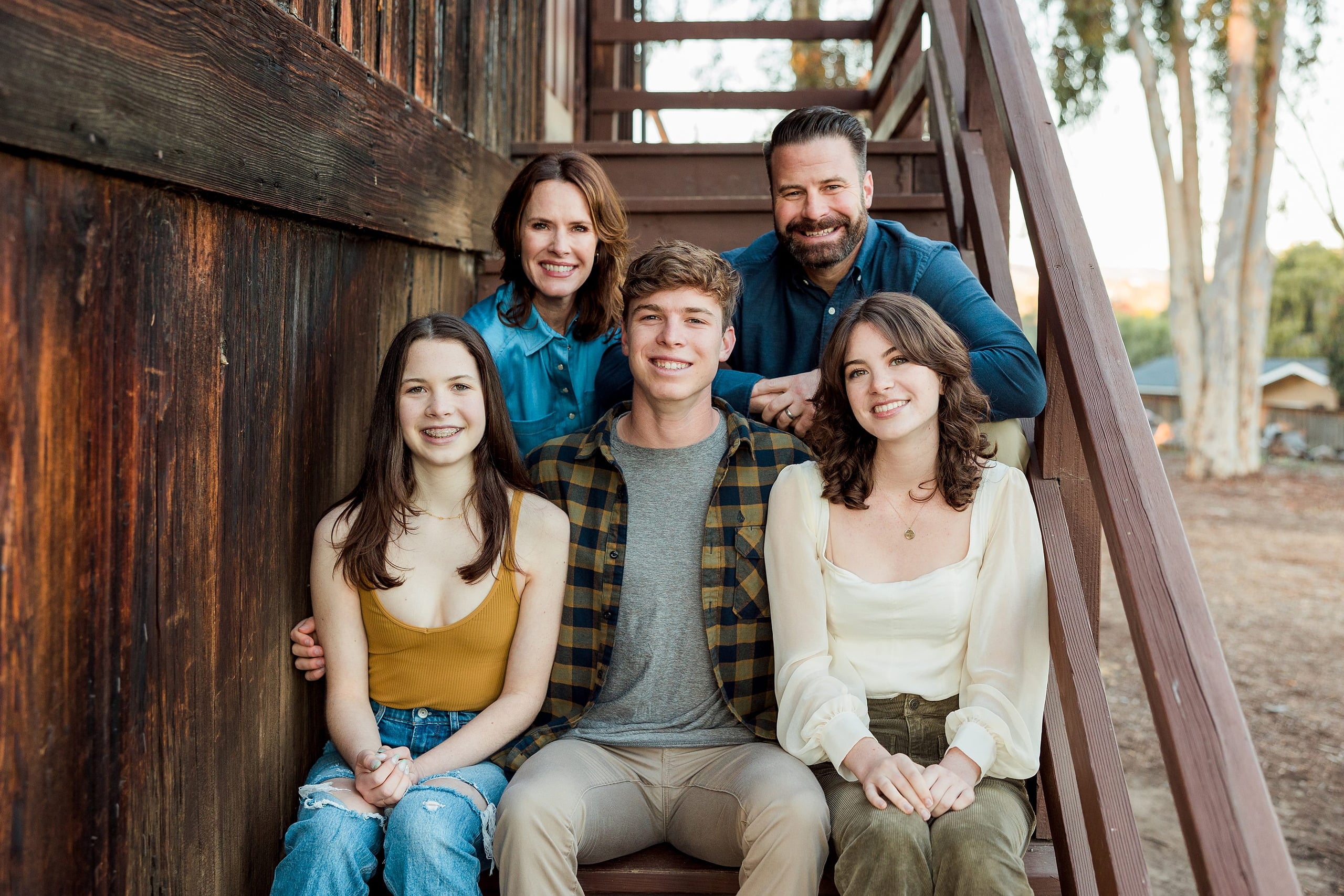 Photographer San Diego — 31 Family of five sitting together on wooden stairs with trees behind