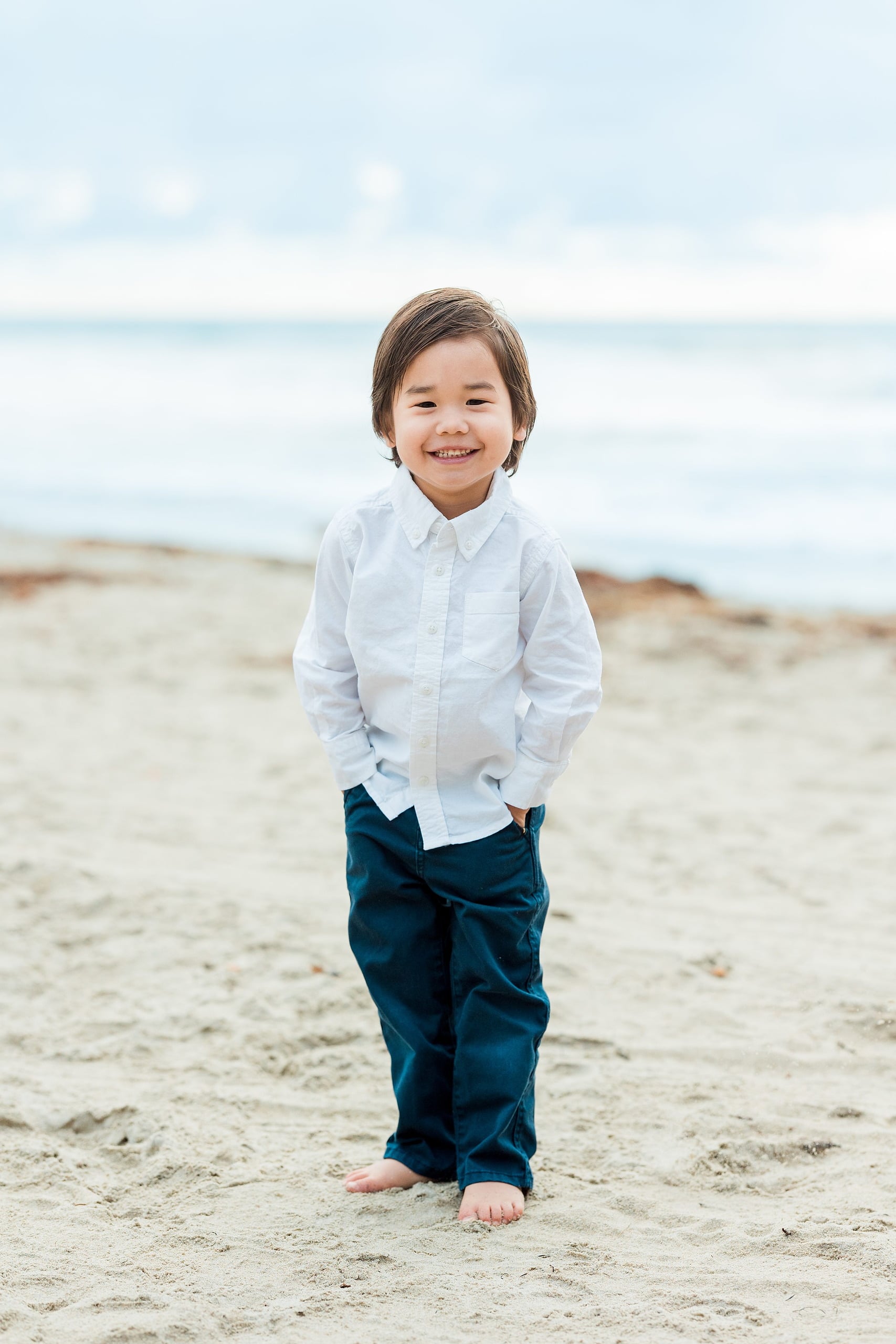 Rainy Day Beach Photo Session — 08 Young man smiles standing on sand with blurred pier and water behind
