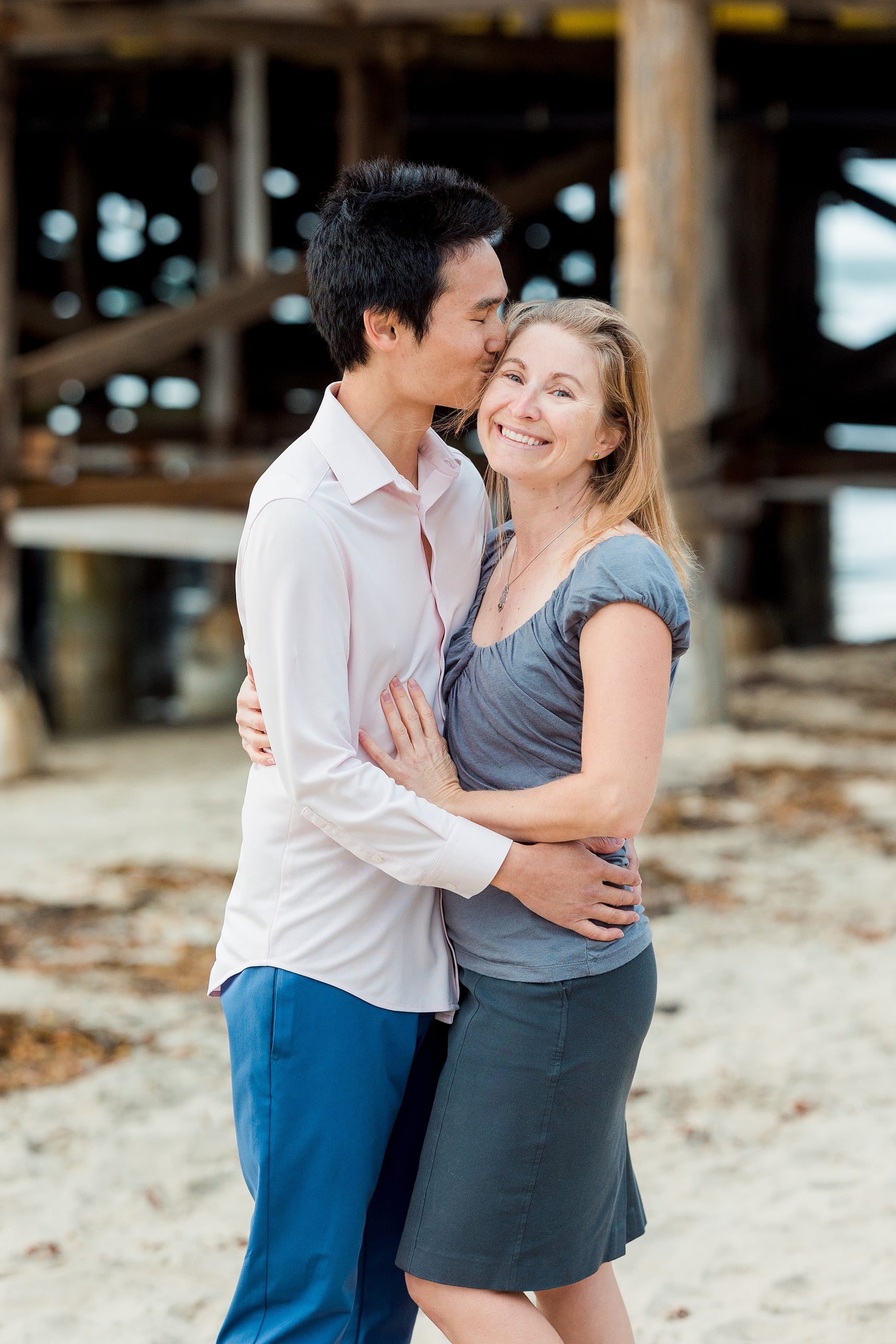 Rainy Day Beach Photo Session — 11 Woman lifts child high in the air on sand with ocean behind them at sunset