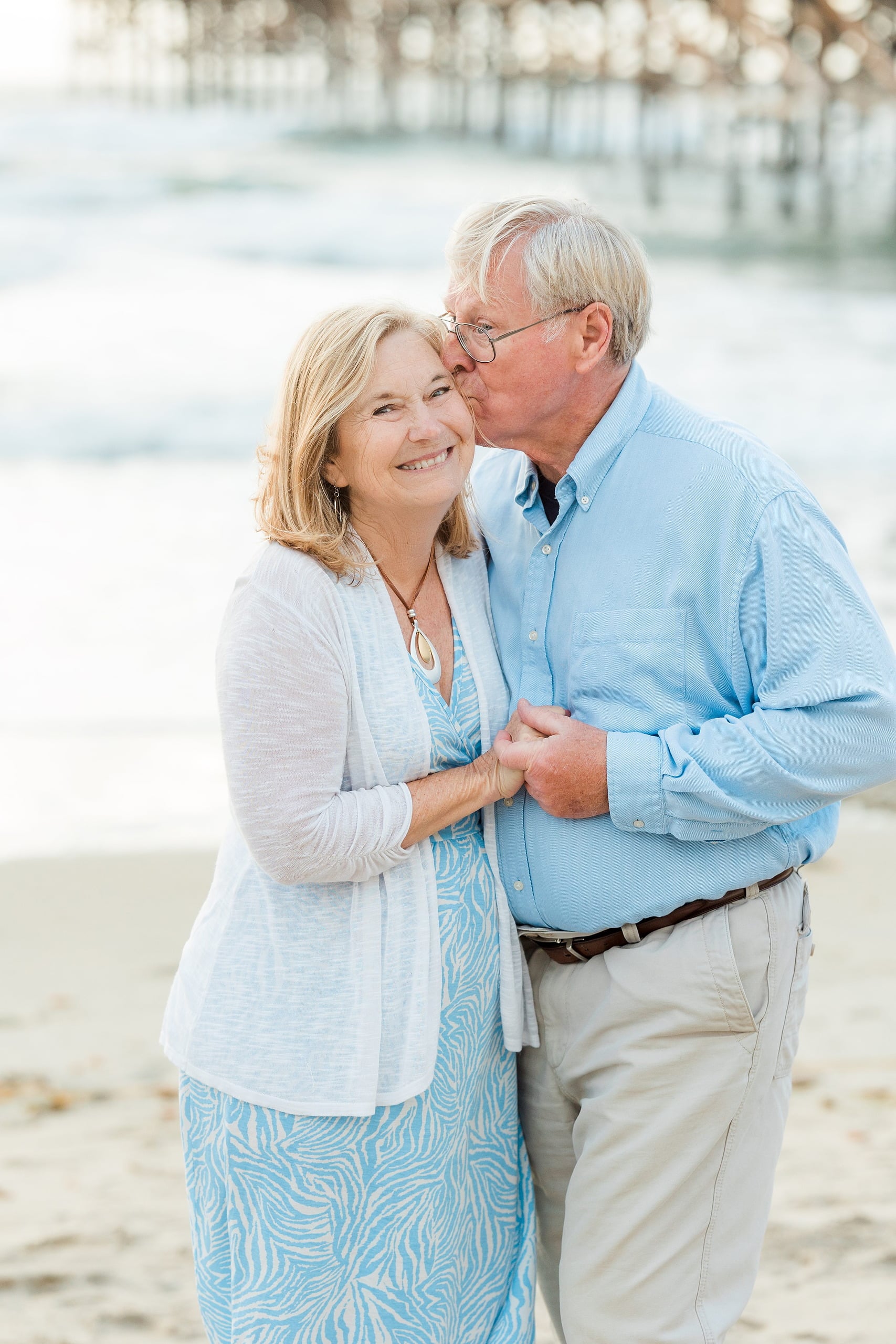 Rainy Day Beach Photo Session — 13 Man and woman embrace while standing on the sand facing each other at the pier