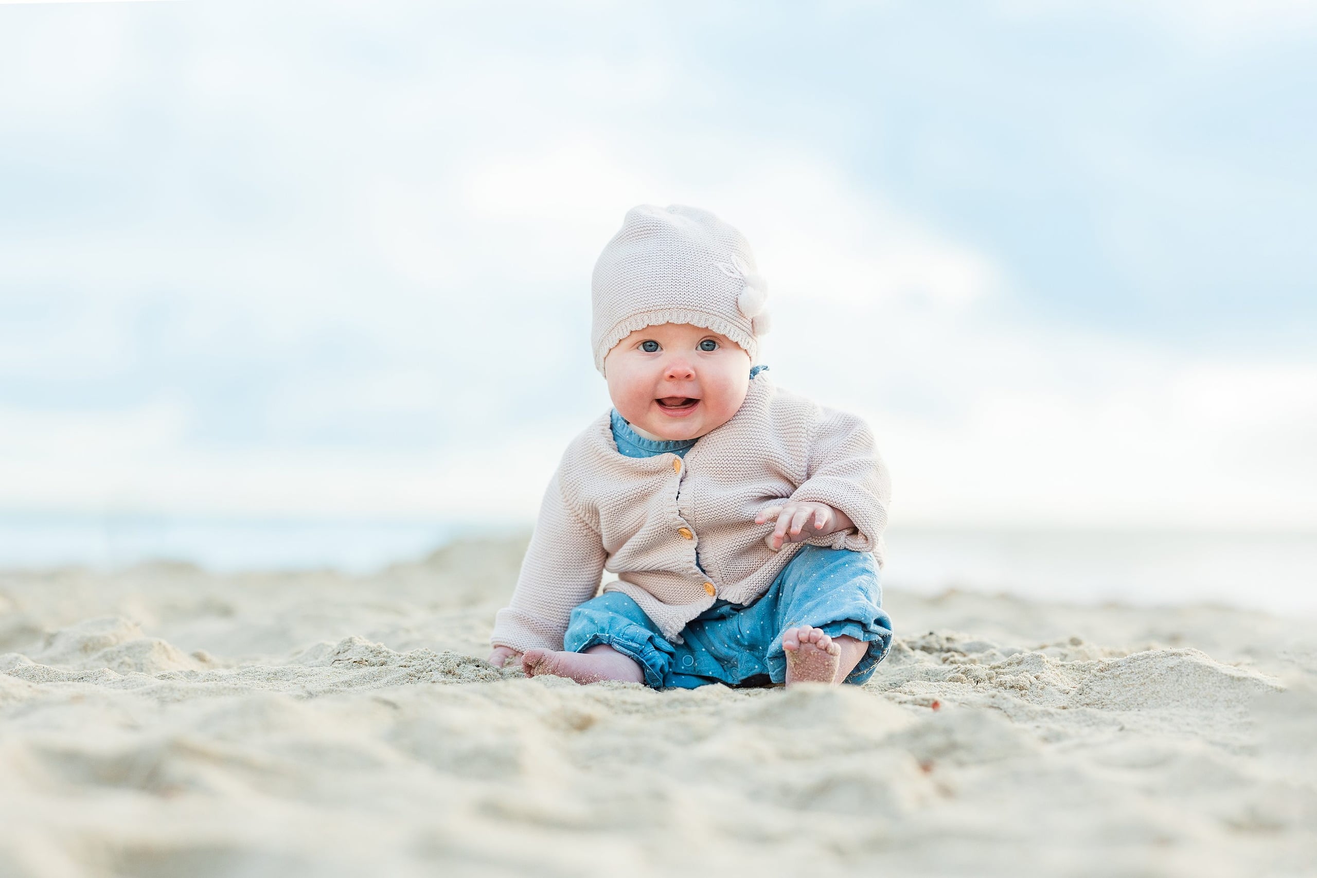 Rainy Day Beach Photo Session — 16 Child sits on the sand in a colorful puffa vest near Crystal Pier Pacific Beach structure