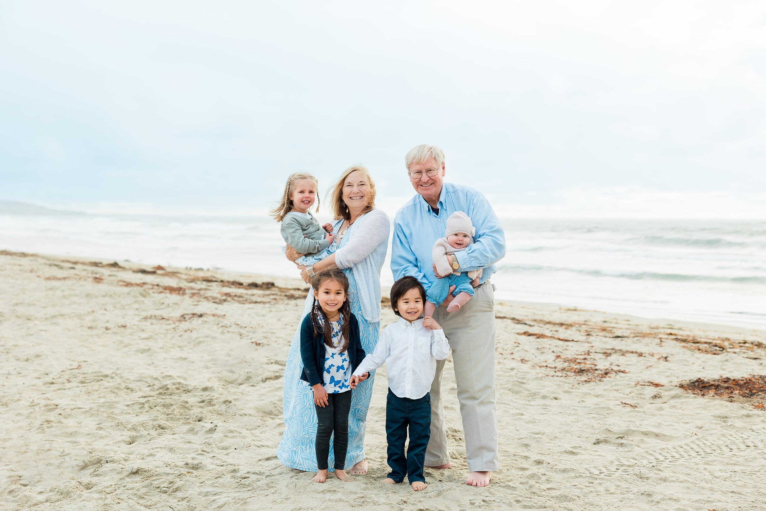 Rainy Day Beach Photo Session — 25 Grandmother carries two young children together while standing in water