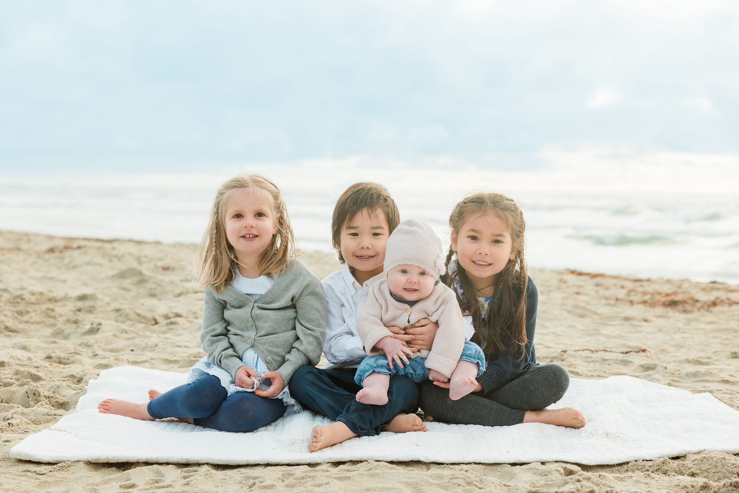 Rainy Day Beach Photo Session — 26 Parents and two children stand holding hands wading through shallow water at the beach