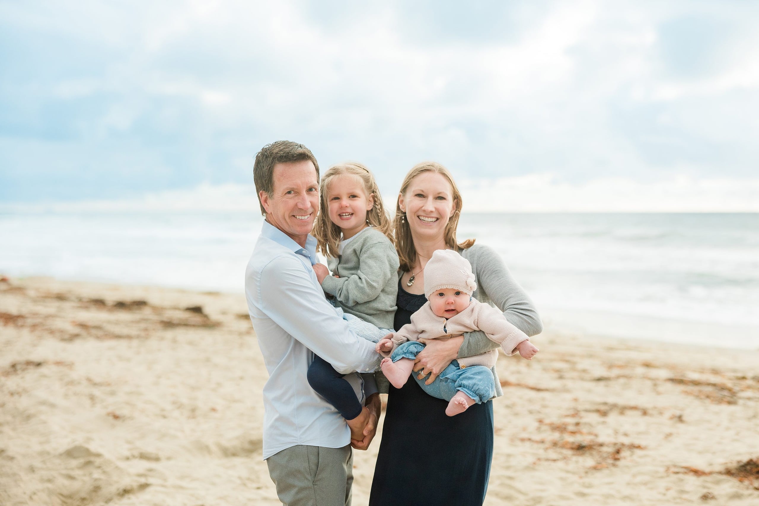 Rainy Day Beach Photo Session — 28 Man stands holding a toddler while woman and child stand beside them on sand
