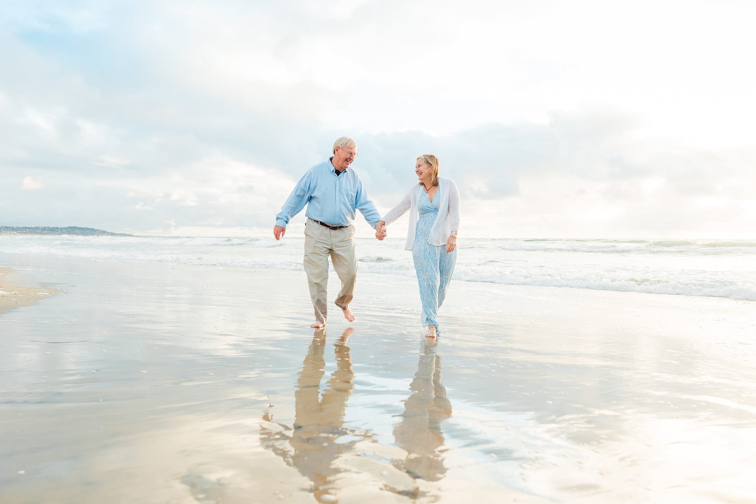 Rainy Day Beach Photo Session — 31 Grandfather and grandmother run hand-in-hand in shallow water on the beach