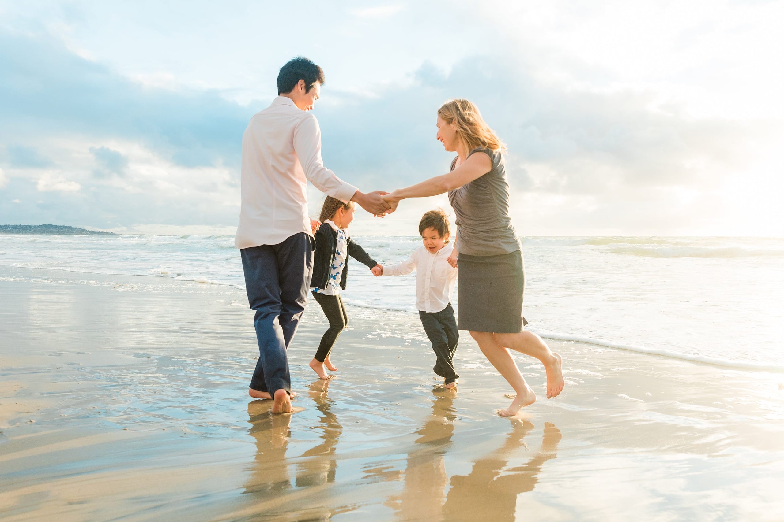 Rainy Day Beach Photo Session — 35 Family of four walk through shallow water holding hands near the pier