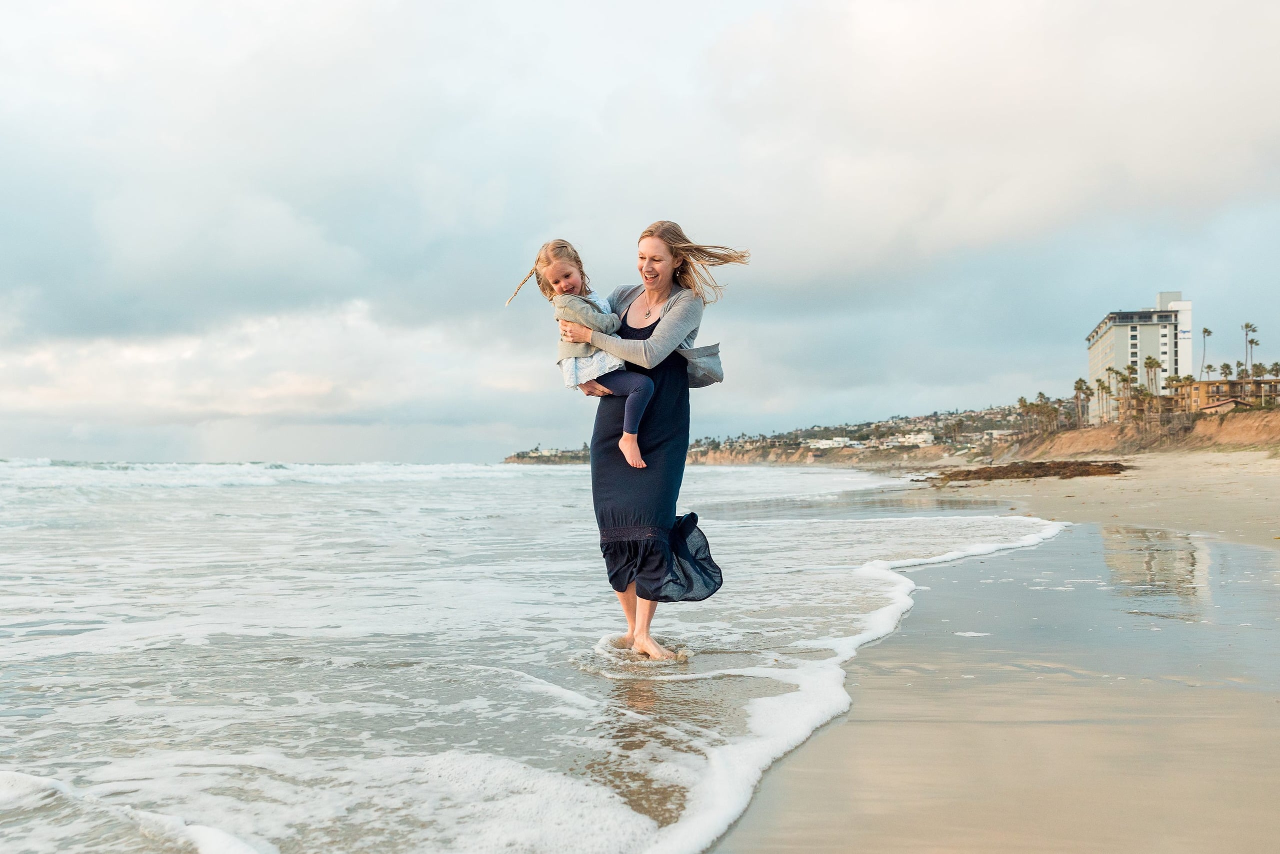 Rainy Day Beach Photo Session — 37 Woman runs holding toddler in her arms through shallow water on the beach