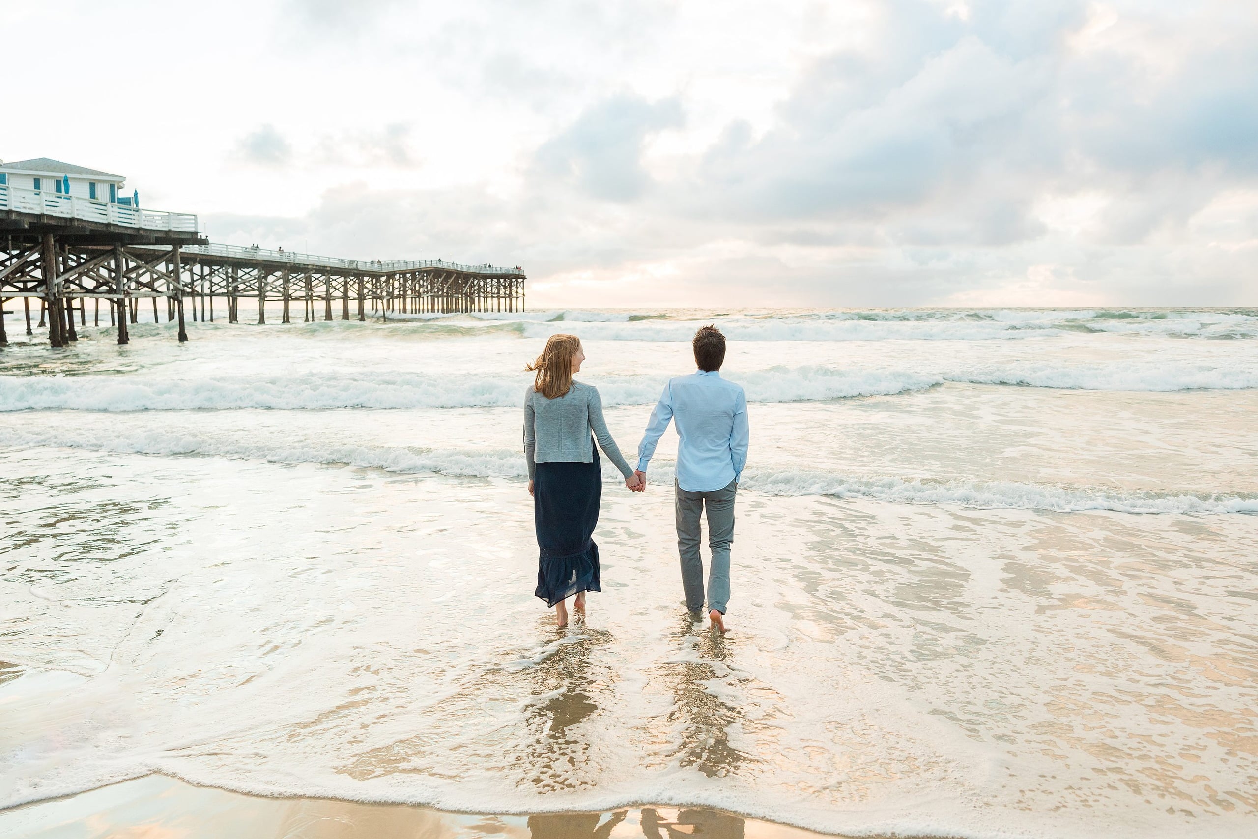 Rainy Day Beach Photo Session — 39 Two children hold hands wading into the ocean water at the beach together