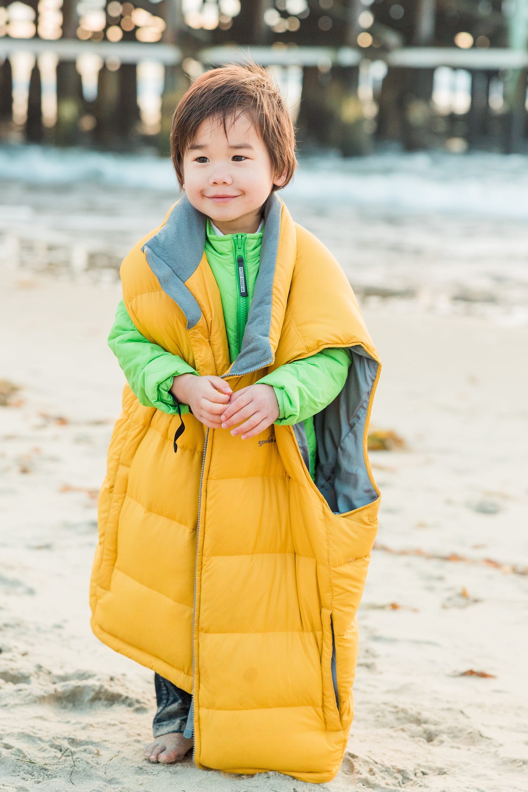 Rainy Day Beach Photo Session — 45 Two young children wrapped together in a colorful puffa vest on the sand