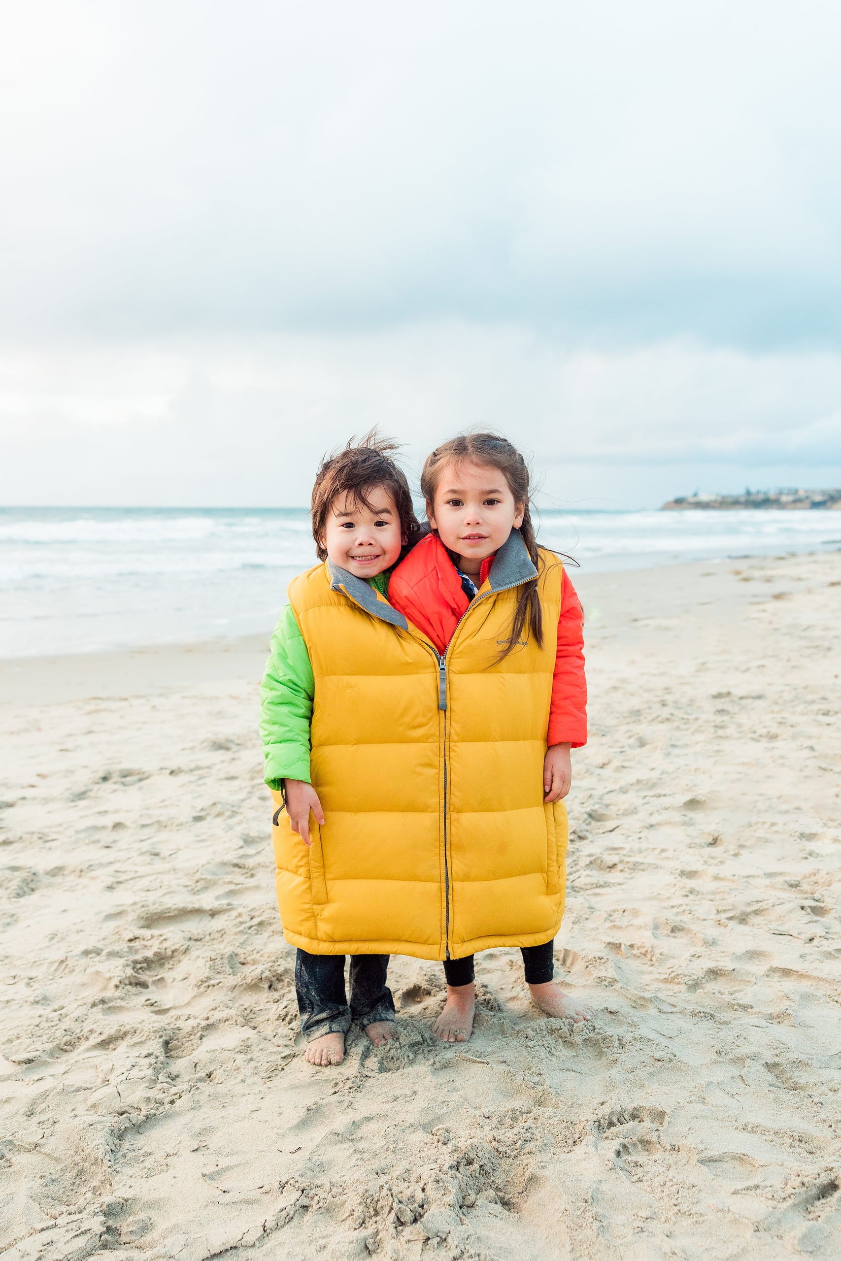 Rainy Day Beach Photo Session — 46 Man holds toy boat while bending toward child wearing yellow puffa vest at beach