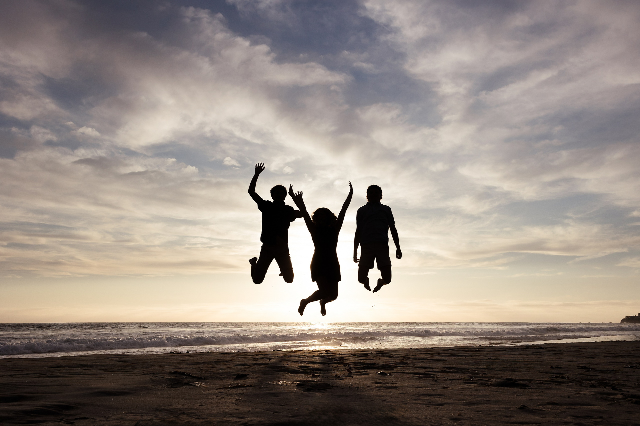 San Diego Beach Family Photos — 16 Three family members jumping silhouetted against dramatic sunset sky