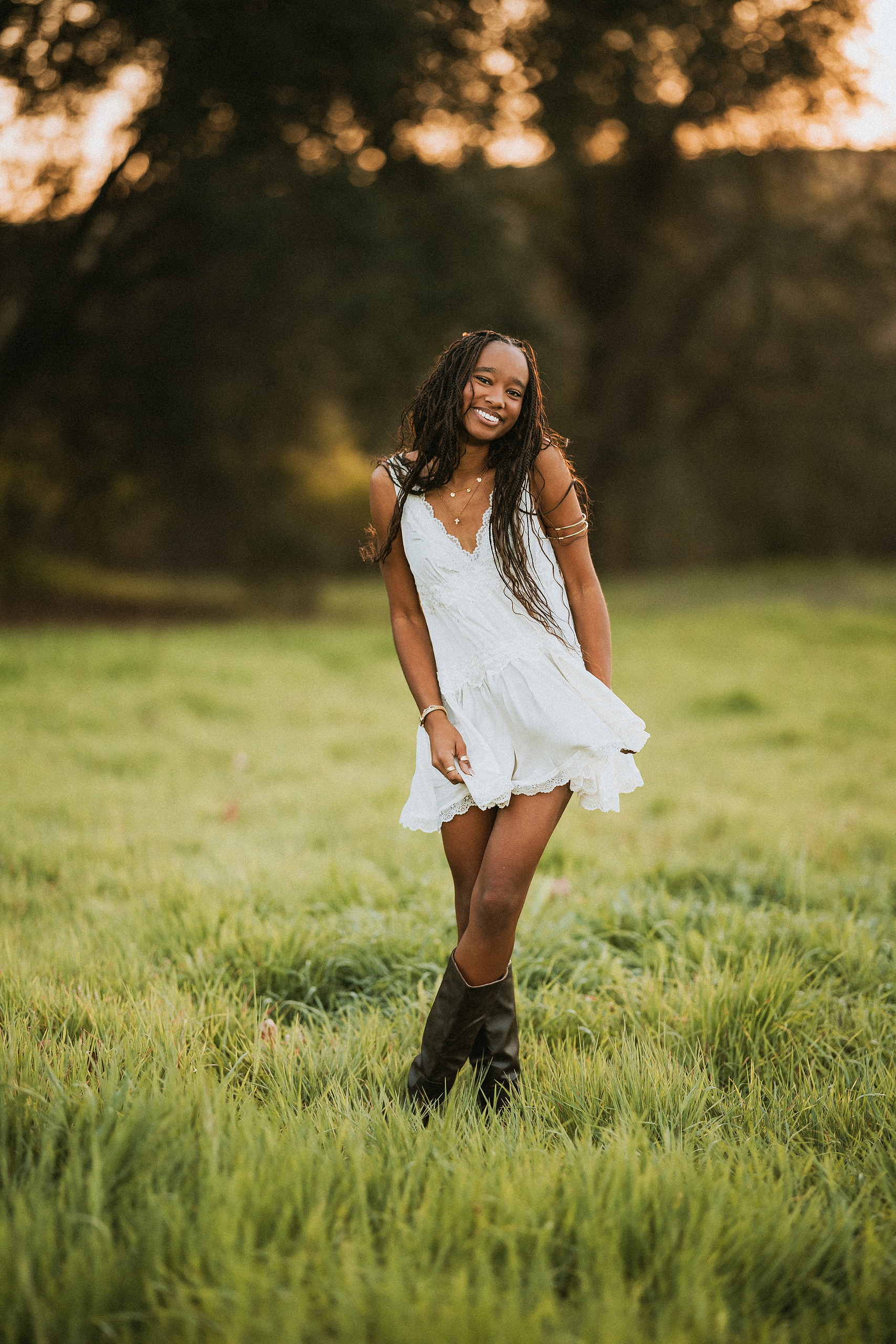 San Diego Senior Photos — 01 Kaelyn standing in white sleeveless dress and black boots, smiling in grassy field