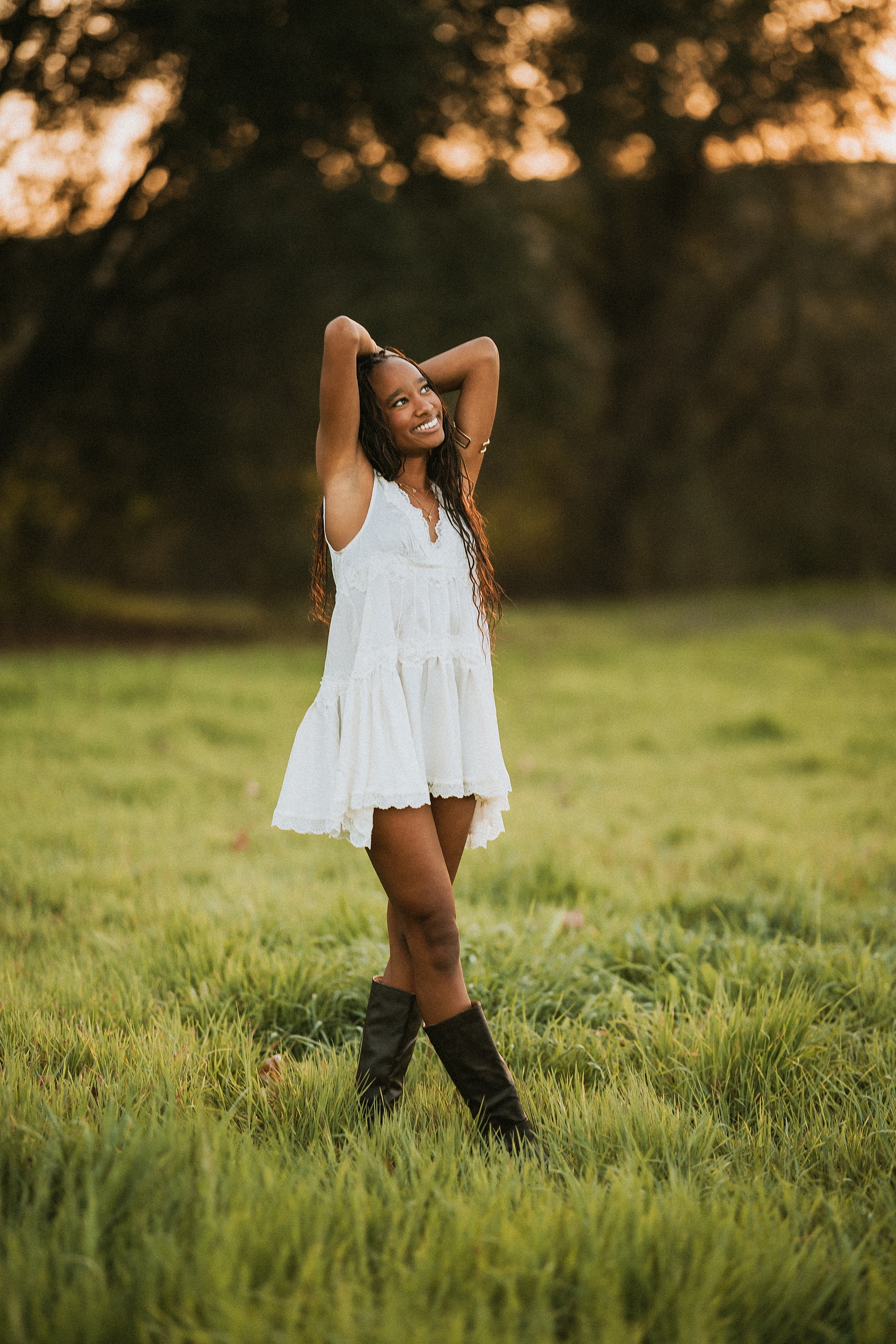 San Diego Senior Photos — 02 Kaelyn in white dress with hands raised behind head, looking up in field
