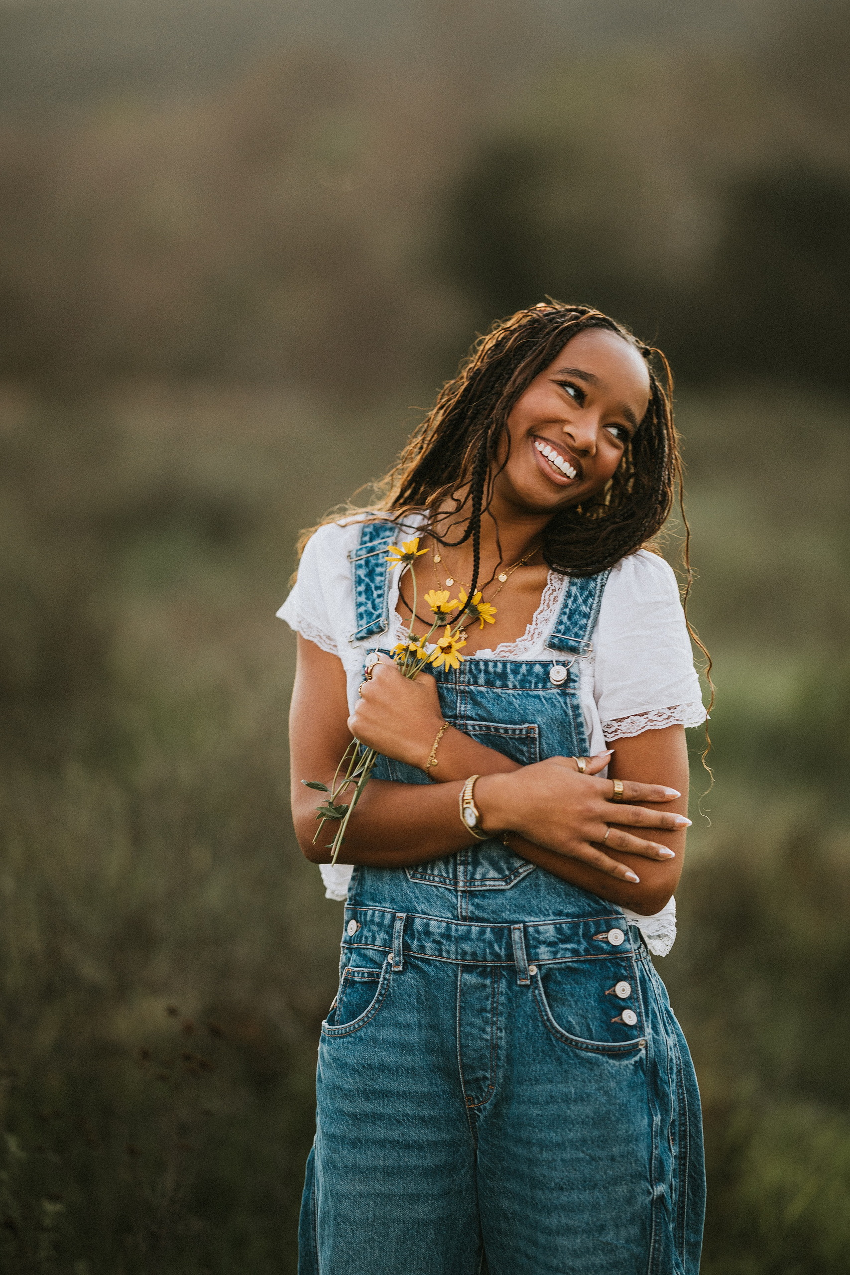 San Diego Senior Photos — 13 Kaelyn in denim overalls and white shirt with arms crossed, holding yellow flowers