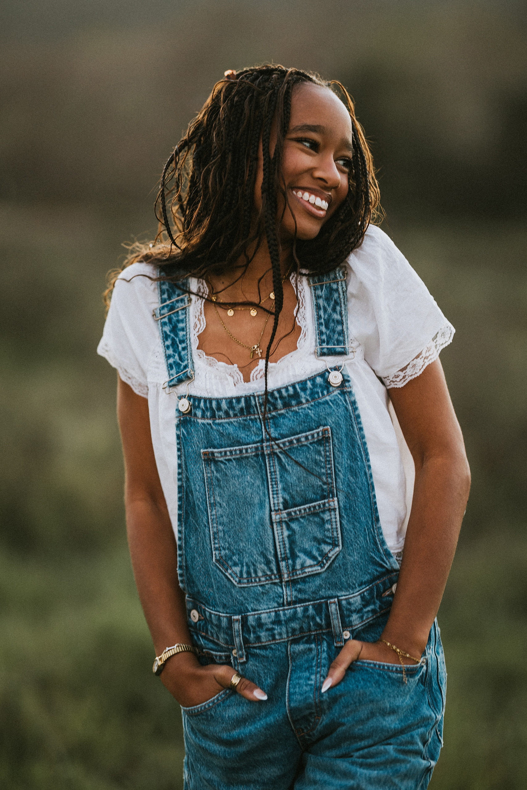San Diego Senior Photos — 16 Kaelyn in denim overalls and white shirt with hand on necklace, smiling