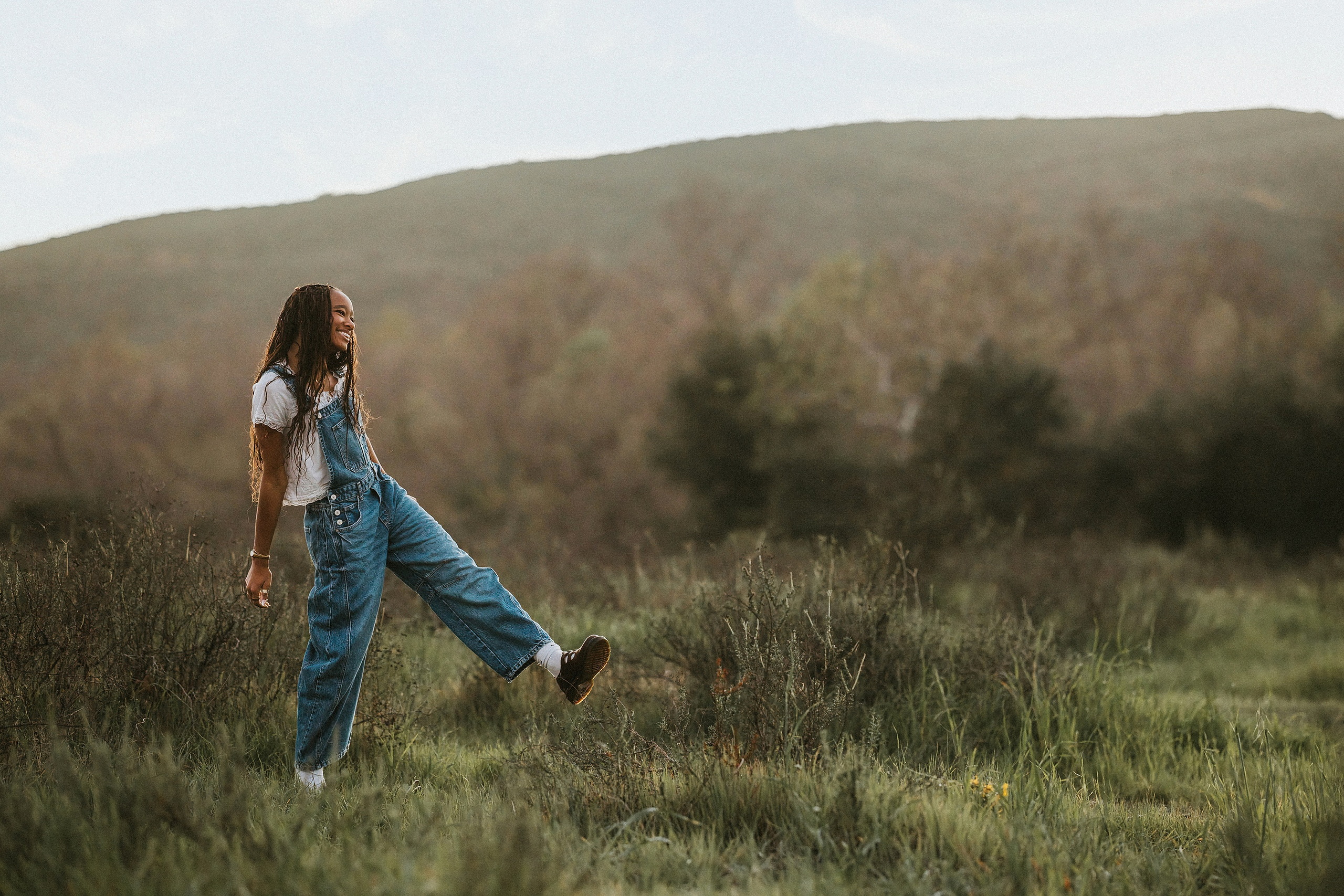 San Diego Senior Photos — 18 Kaelyn in white dress crouching on rock in field with trees behind